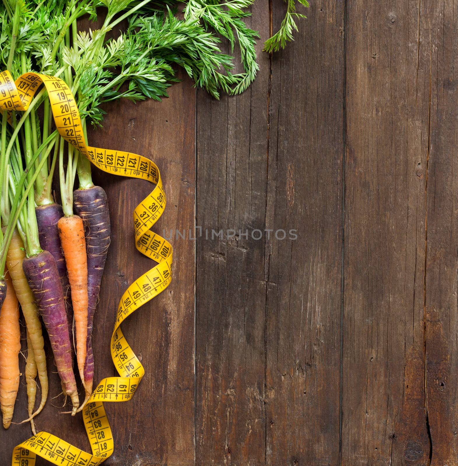 Fresh organic rainbow carrots and yellow measuring type on wood