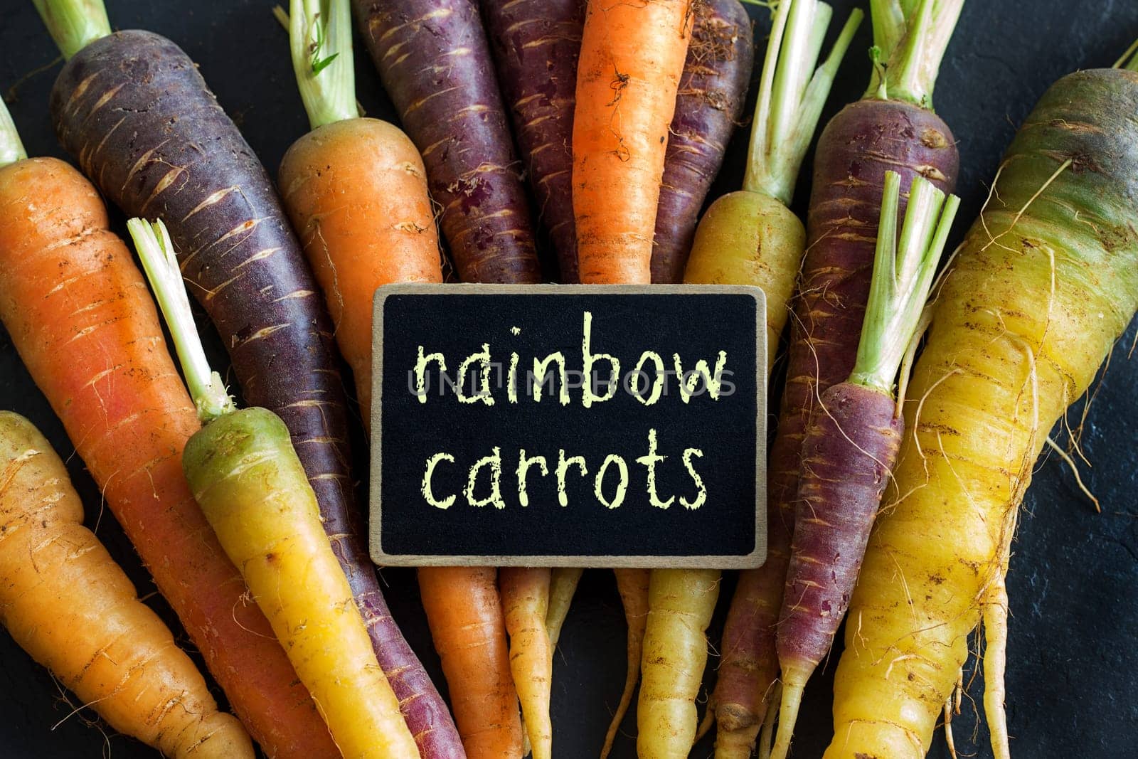 Fresh organic rainbow carrots and a small chalkboard on wood