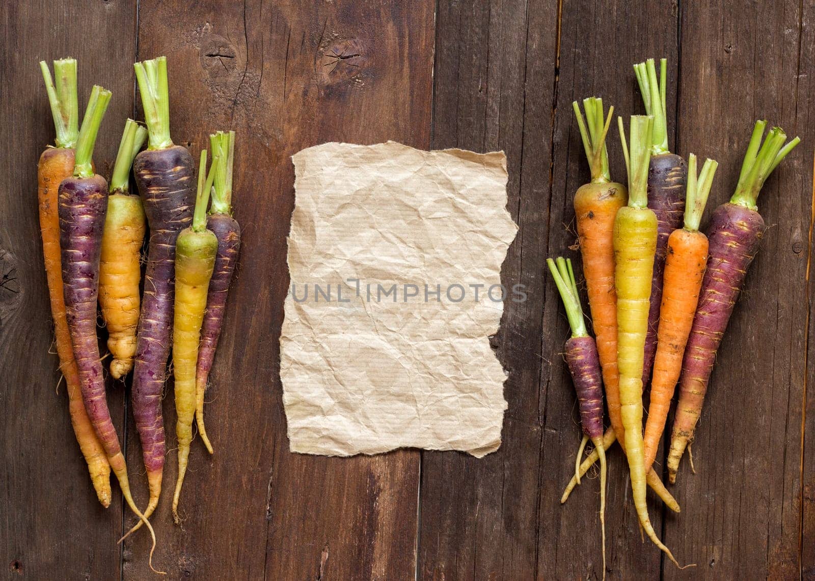 Fresh organic rainbow carrots and craft paper on wood