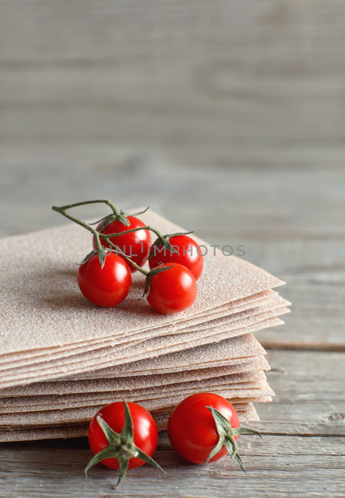 Raw lasagna sheets and cherry tomatoes on a wooden table close up