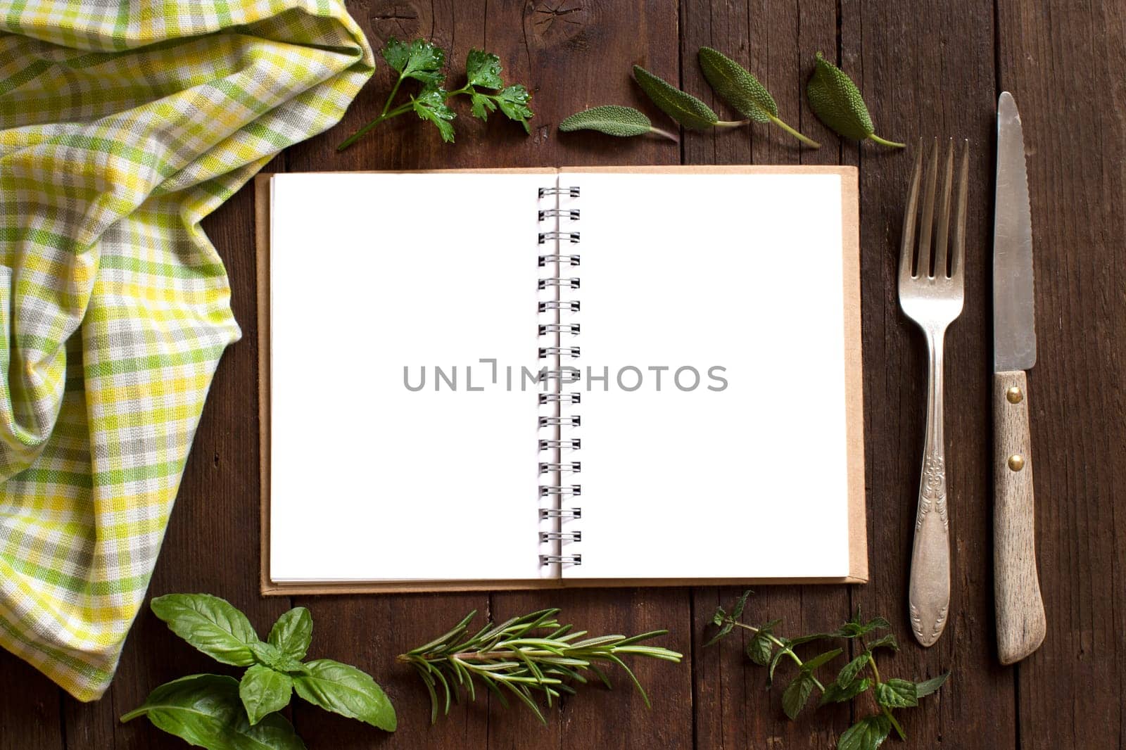 Blank cooking recipe book with fork, knife, herbs and napkin on a wooden table