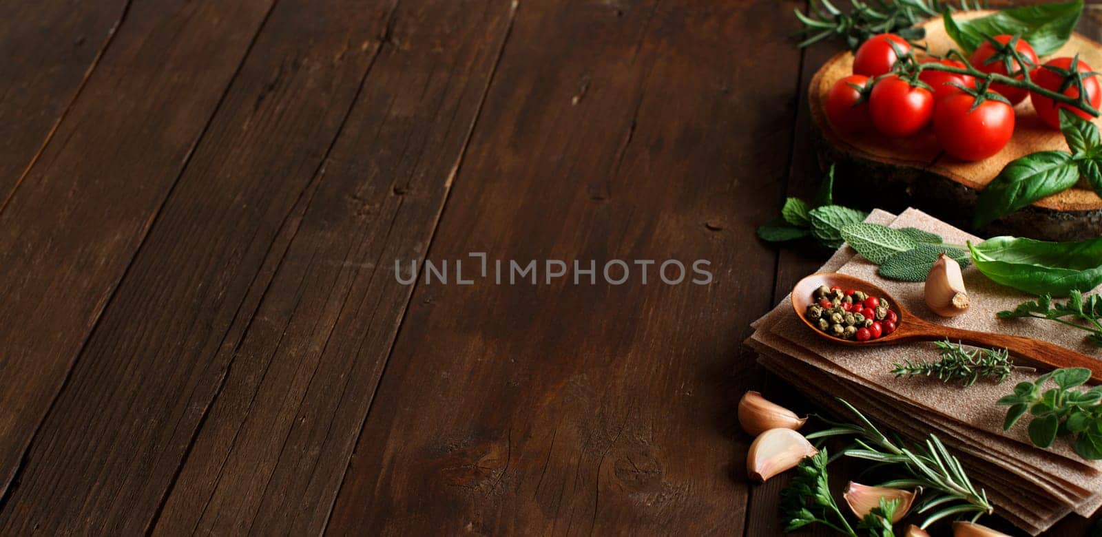Raw lasagna pasta, vegetables and herbs on a wooden background