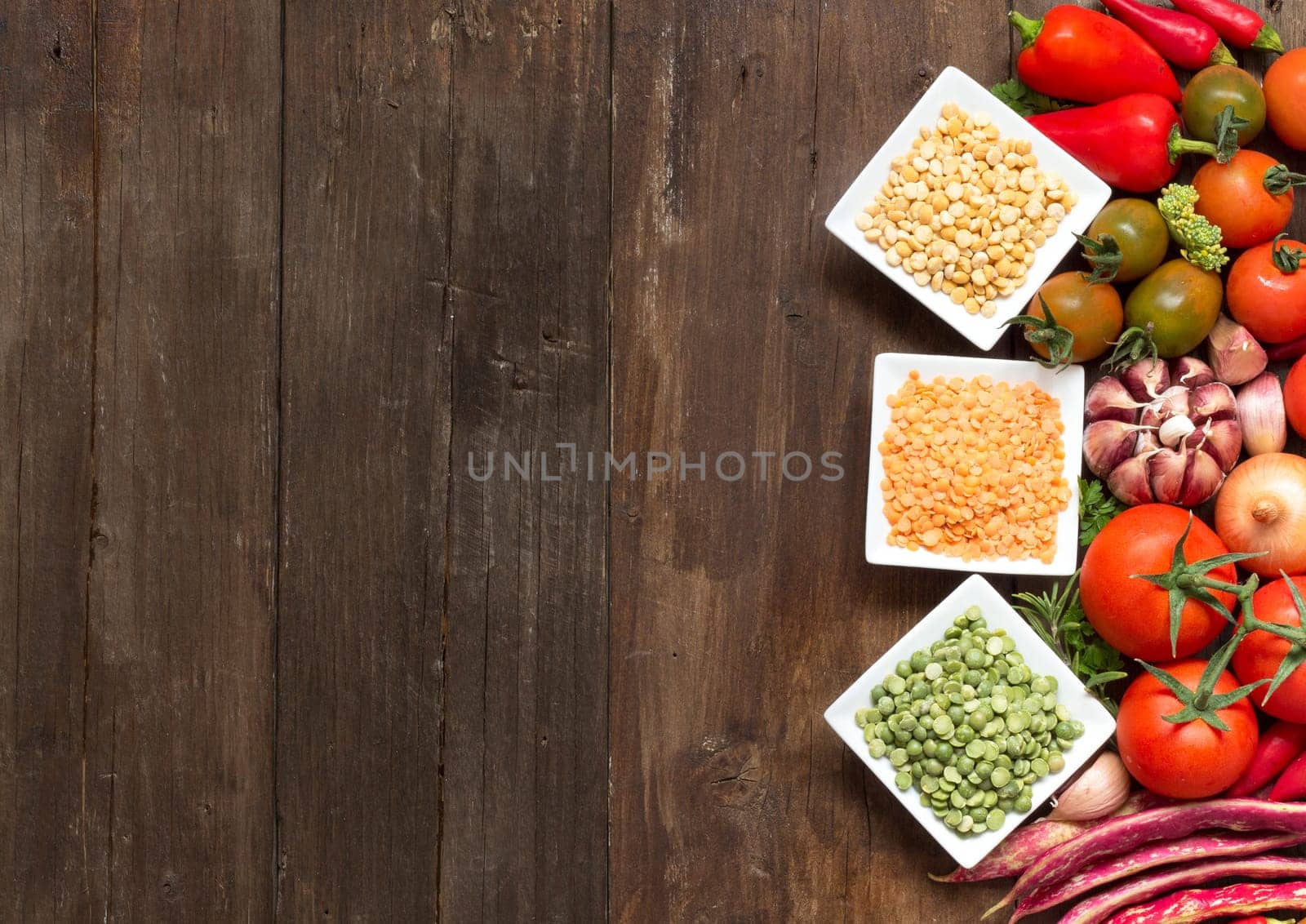 Legumes in bowls and vegetables on a wooden table