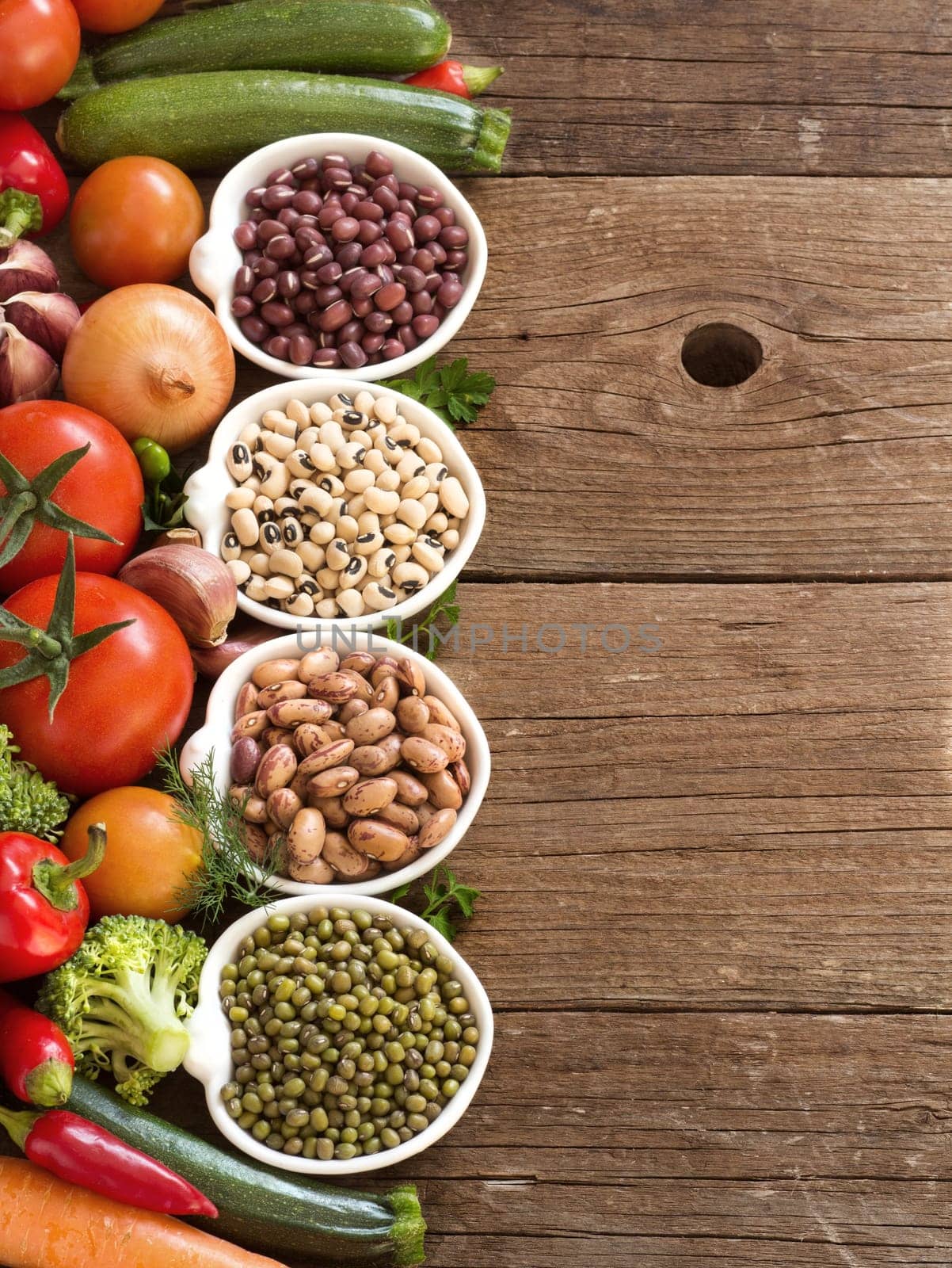 Legumes in bowls and vegetables on a wooden table