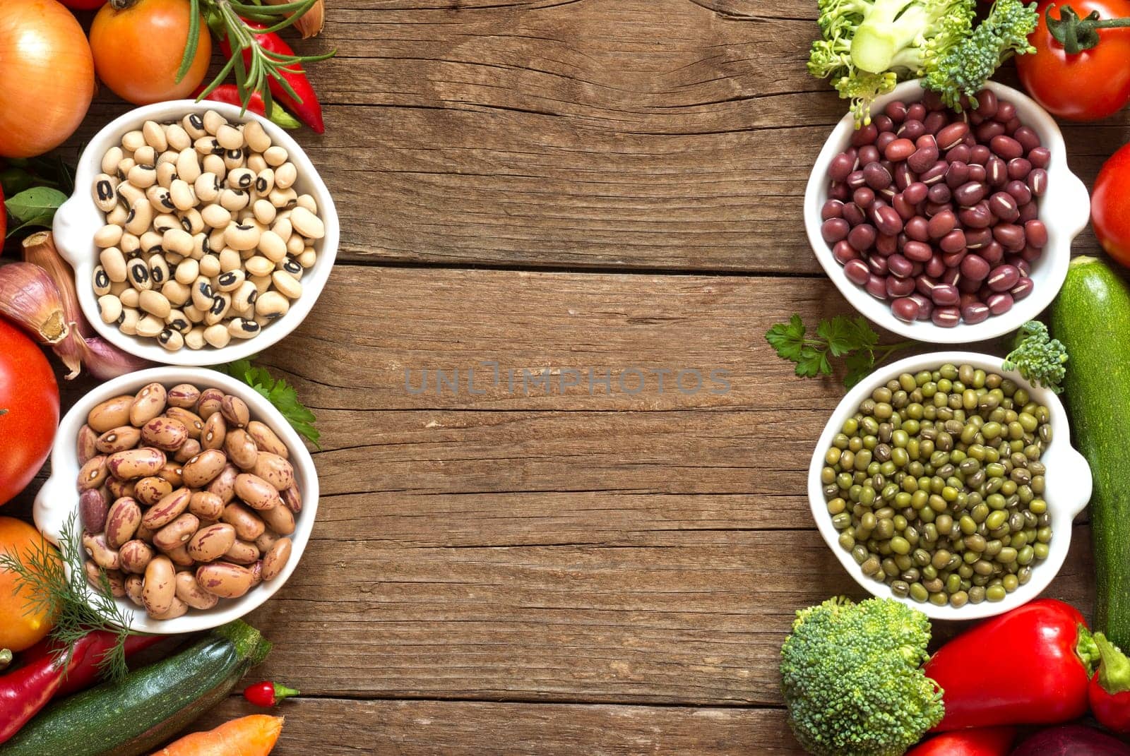 Legumes in bowls and vegetables on a wooden table