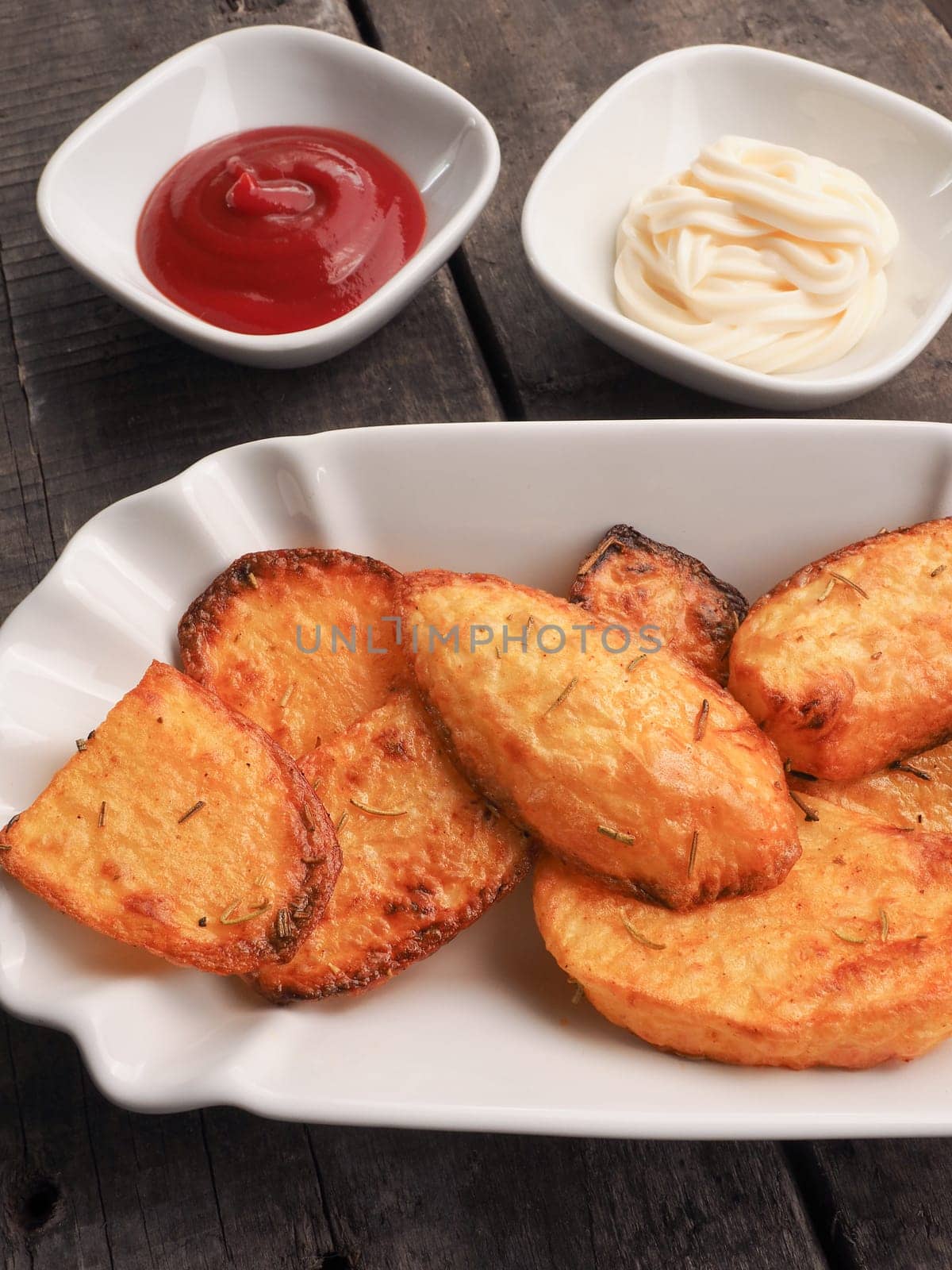 Rosemary potatoes with ketchup and mayonnaise on an old wooden kitchen table