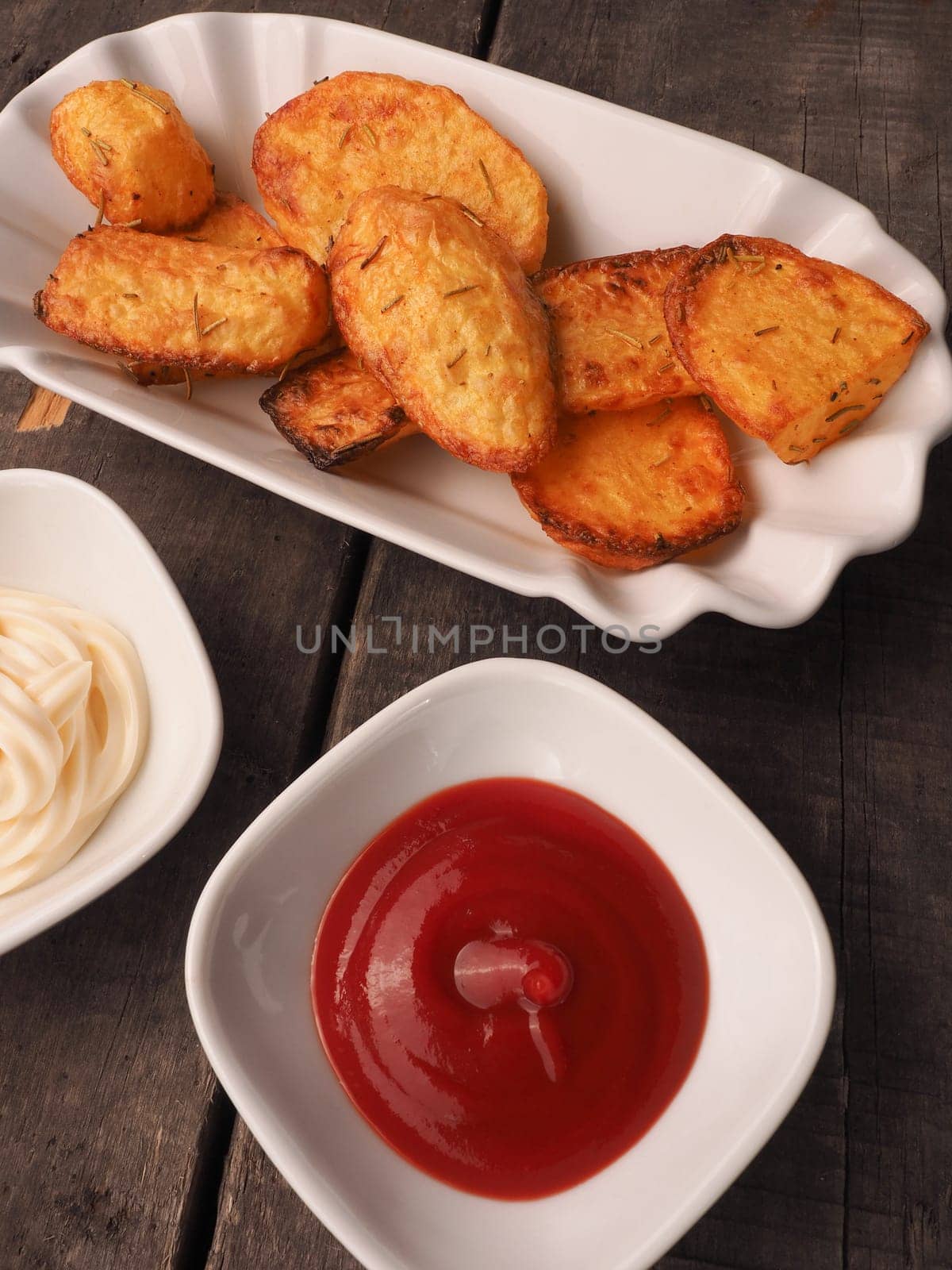 Rosemary potatoes with ketchup and mayonnaise on a rustic wooden table