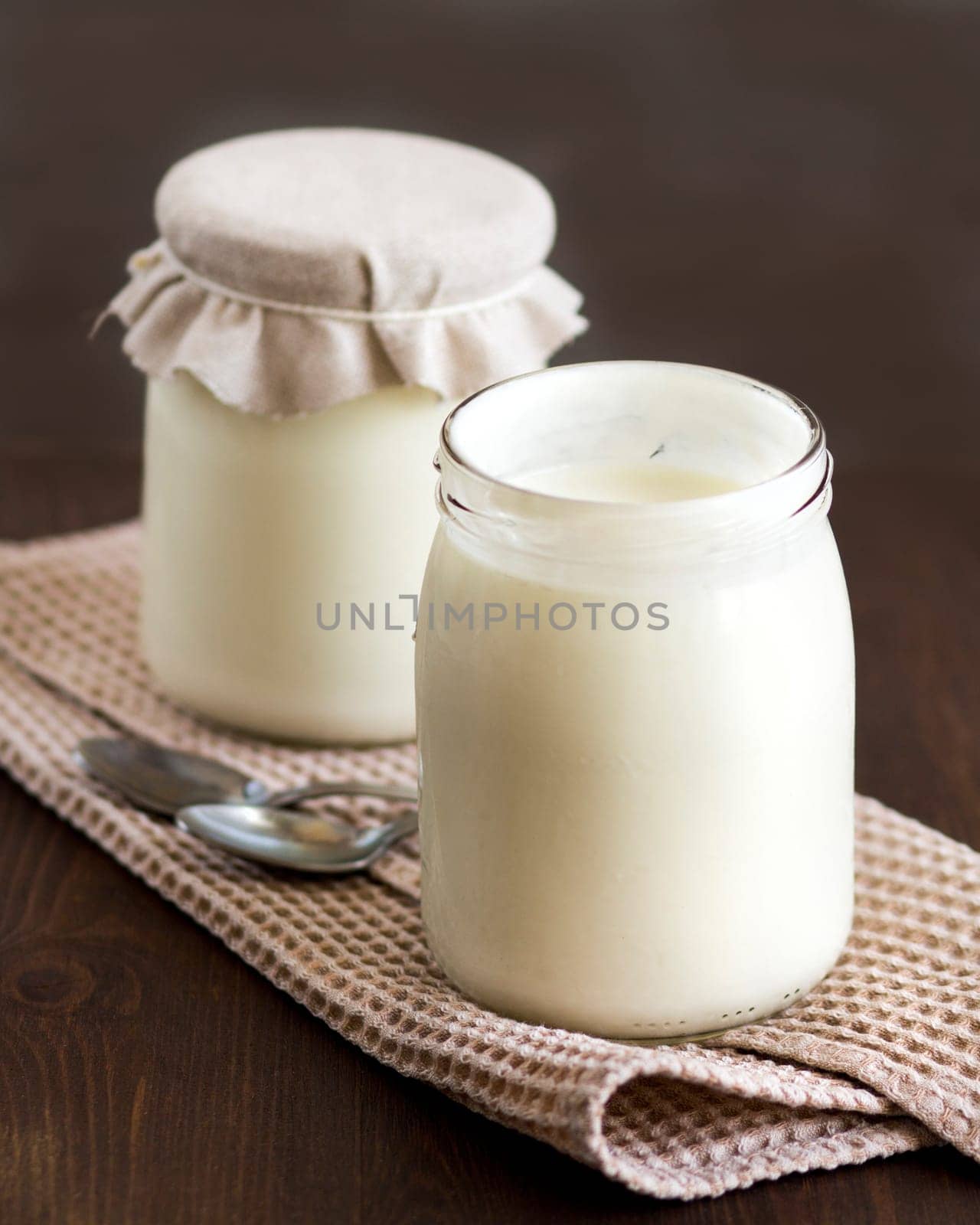 Jars of fresh natural yogurt with spoons on wooden background