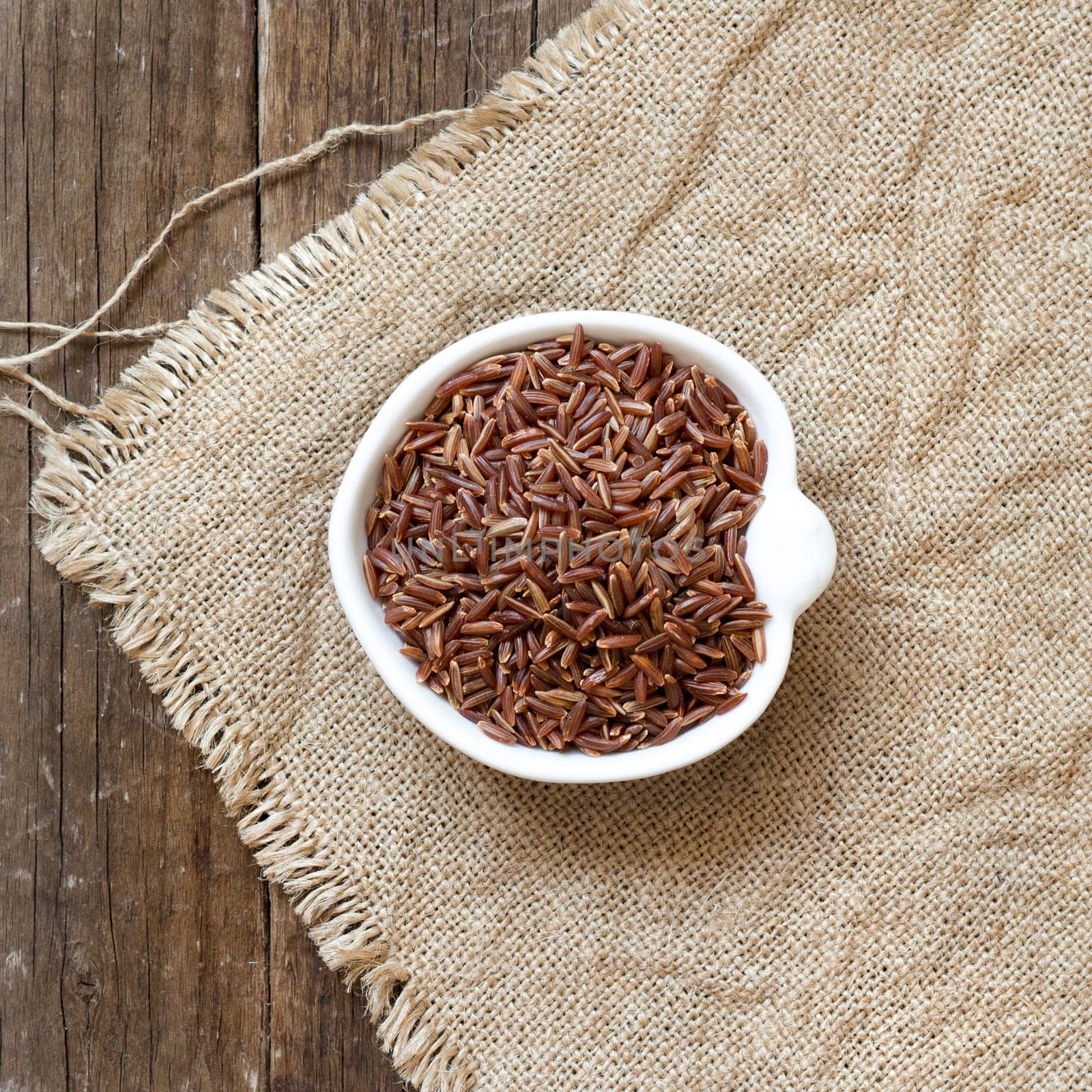 Raw red rice in a bowl on burlap