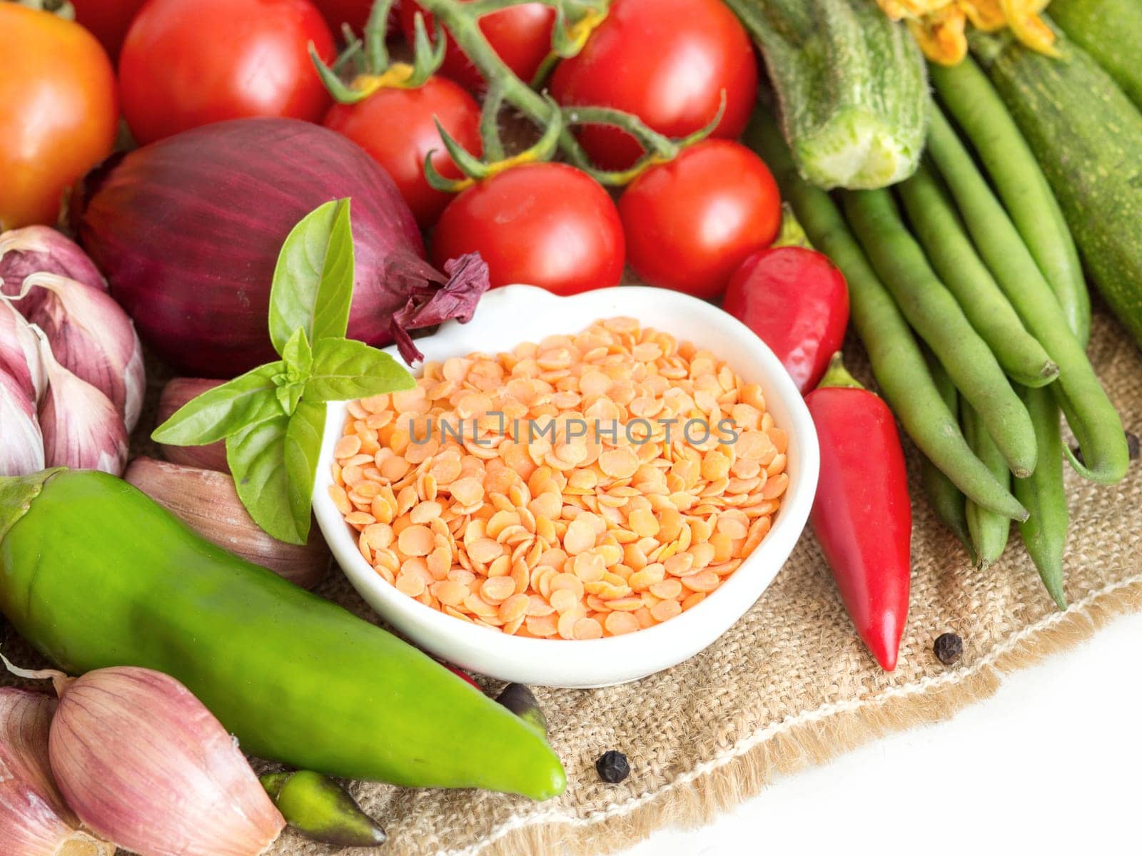 Red lentils in bowl and vegetables isolated on white