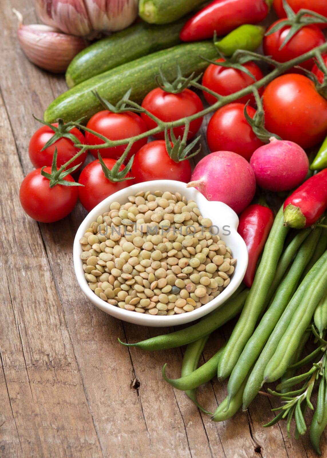 Green lentils in bowl and vegetables on a wooden table