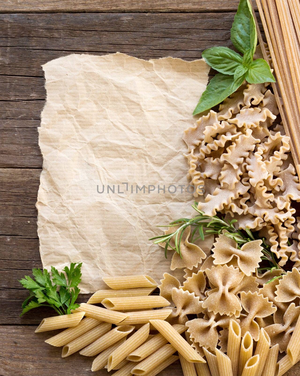 Pasta, herbs and paper on wooden background