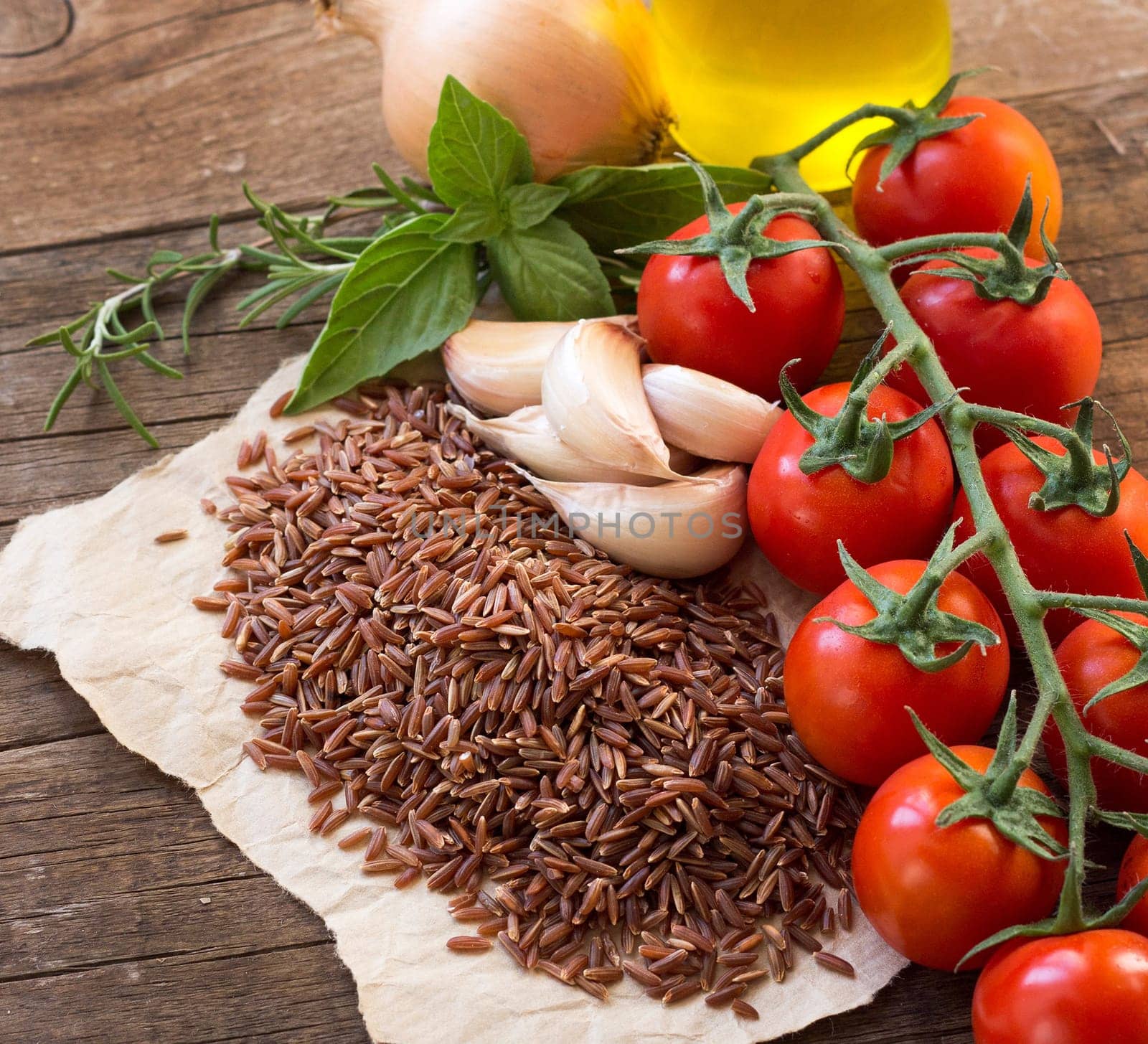 Organic red rice, tomatoes, olive oil, garlic and herbs on wooden background