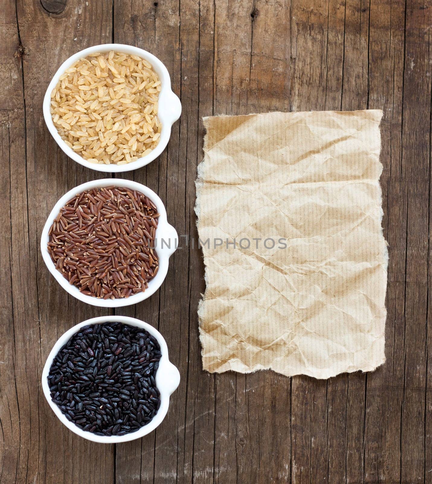 Variety of rice in bowls on wooden table and old paper