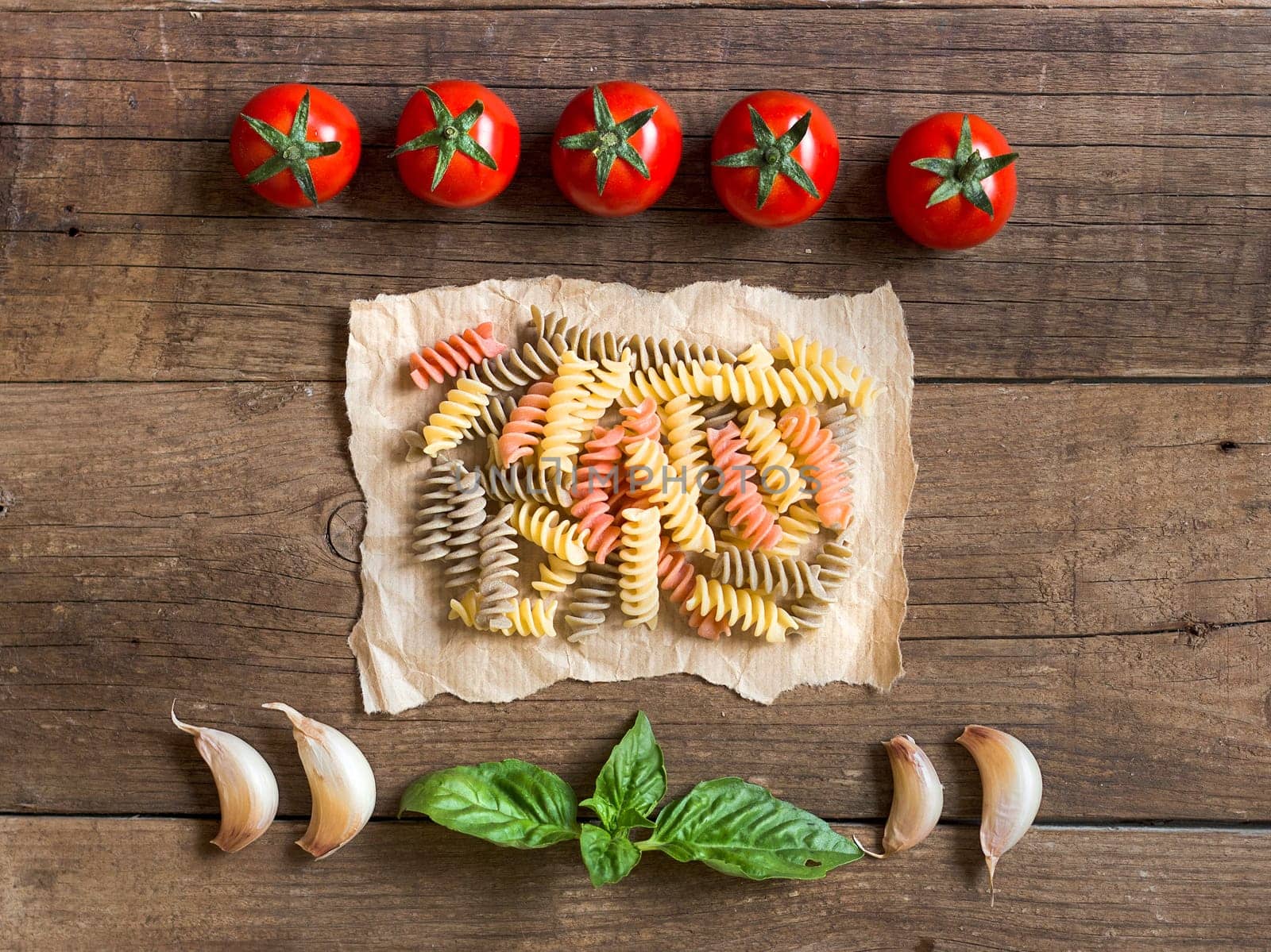 Pasta, tomatoes, garlic and basil on wooden background