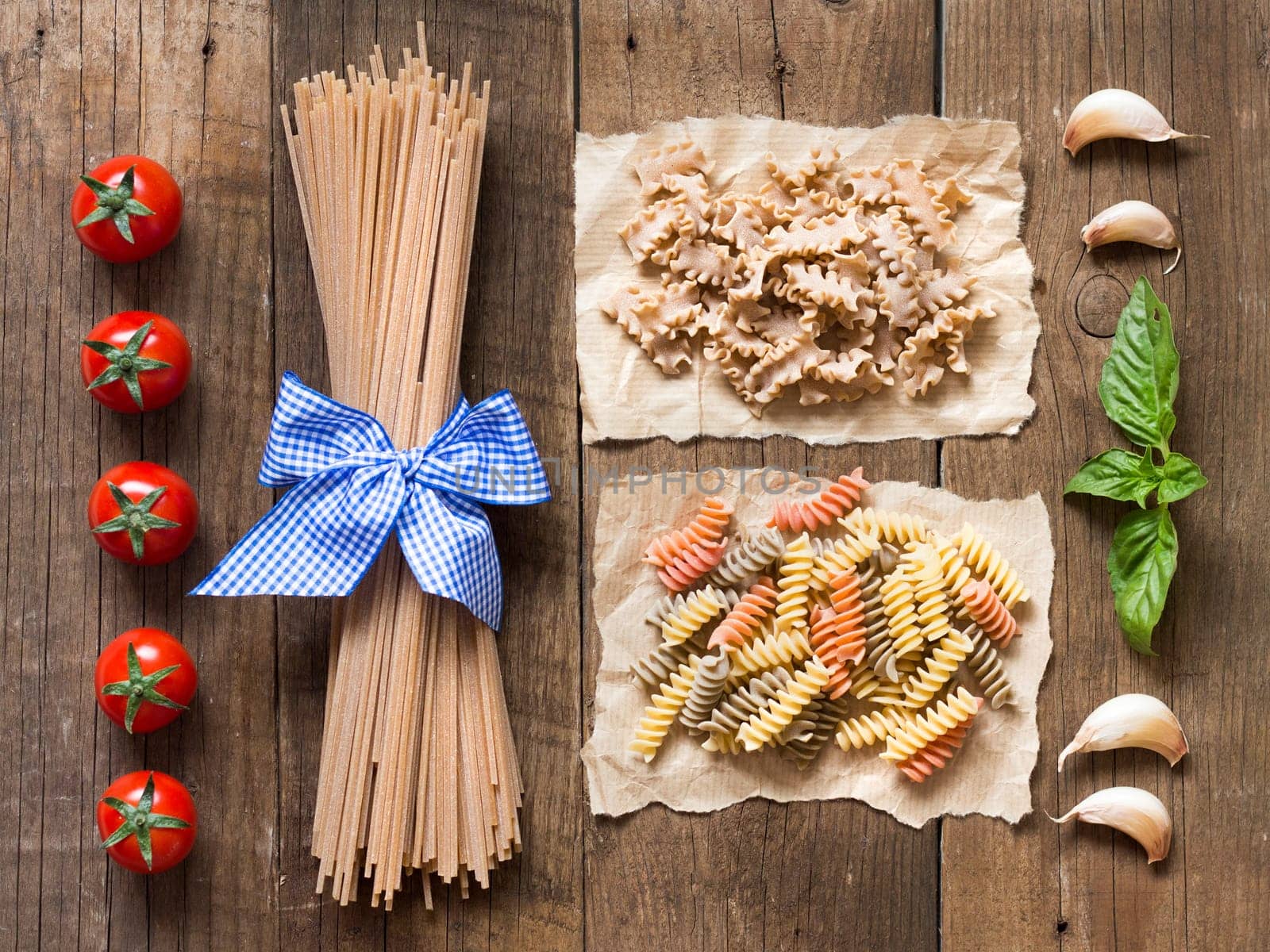 Pasta, tomatoes, garlic and basil on wooden background