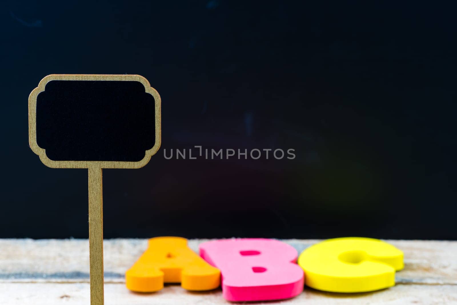 Wooden mini blackboard label over chalkboard background and table with letters ABC, copy space available, education concept