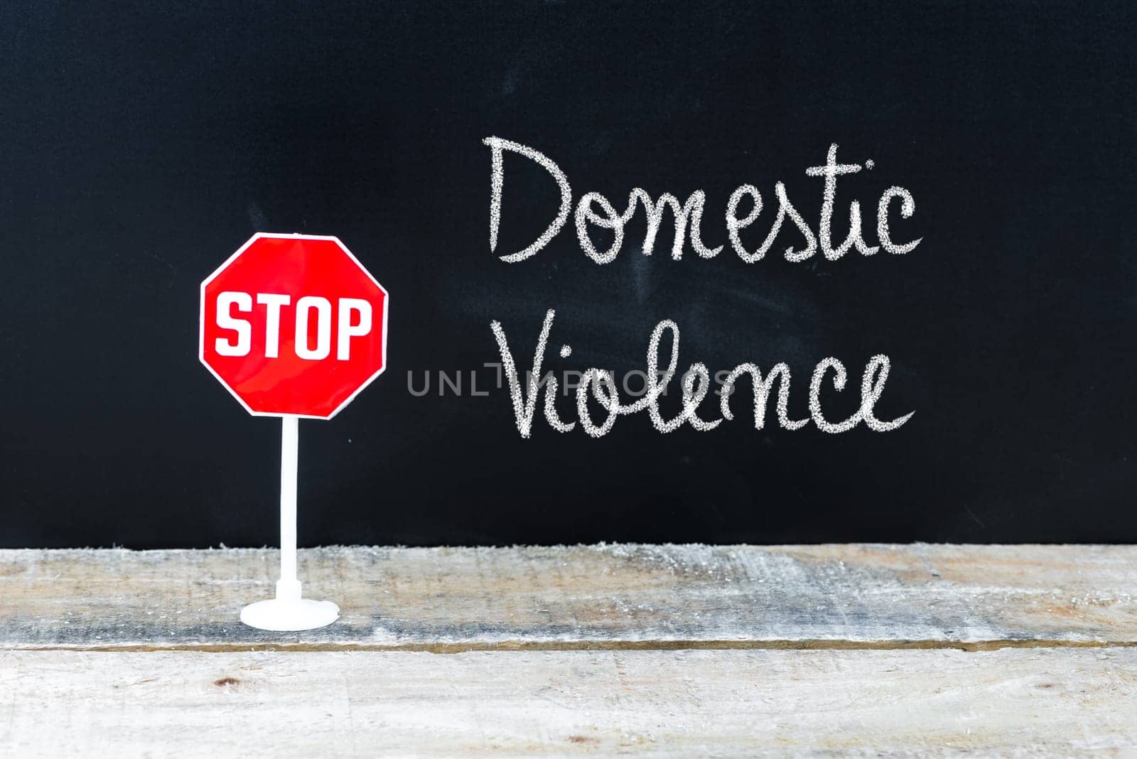 Mini STOP sign over chalkboard background and table, STOP DOMESTIC VIOLENCE concept
