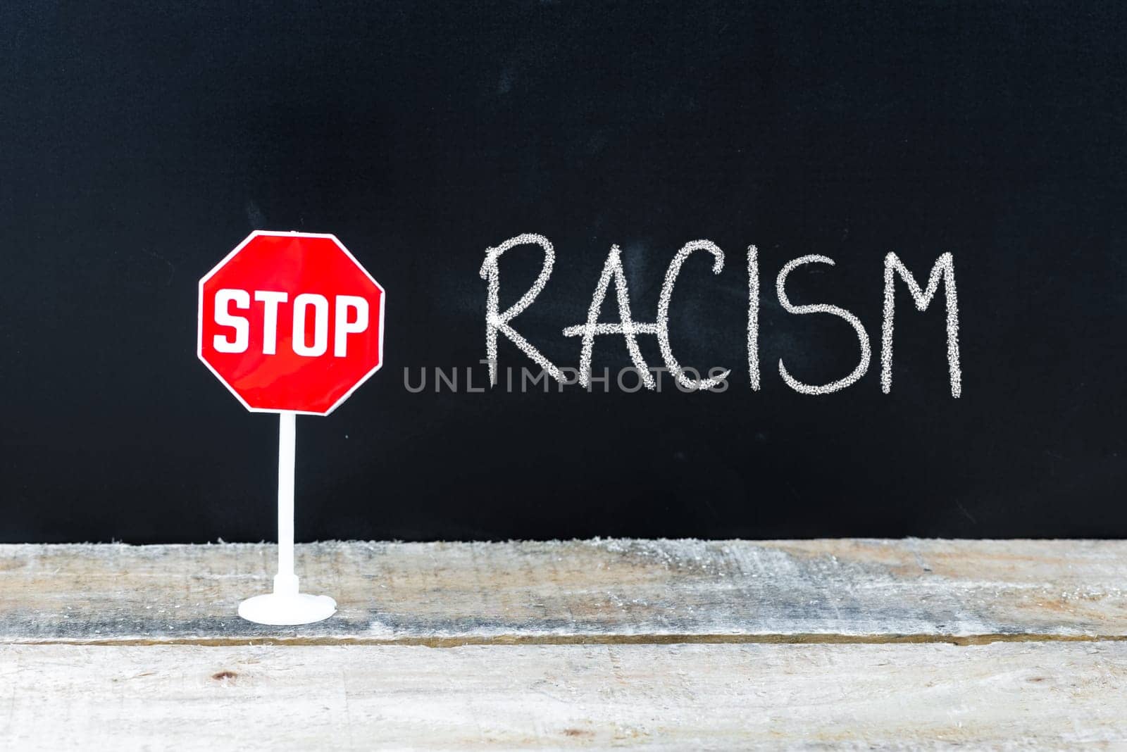 Mini STOP sign over chalkboard background and table, STOP RACISM concept