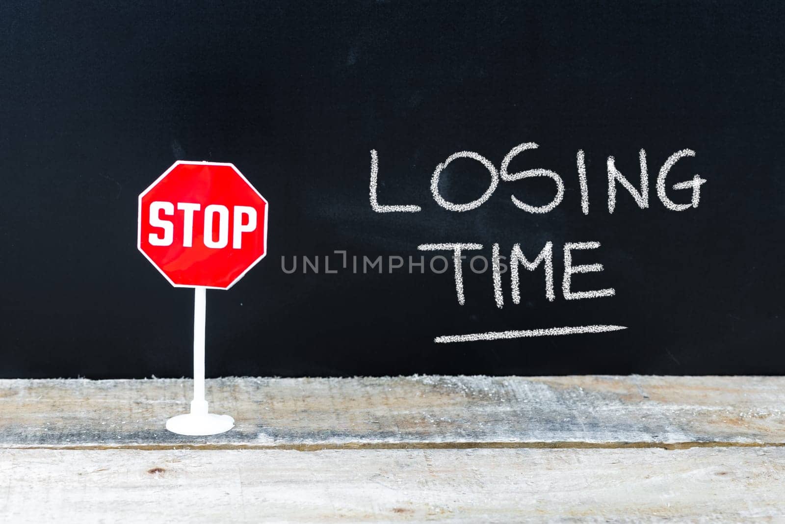 Mini STOP sign over chalkboard background and table, STOP LOSING TIME concept