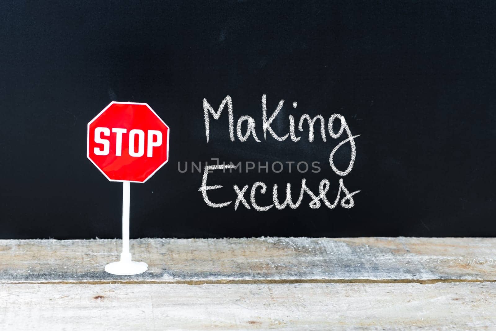Mini STOP sign over chalkboard background and table, STOP MAKING EXCUSES concept