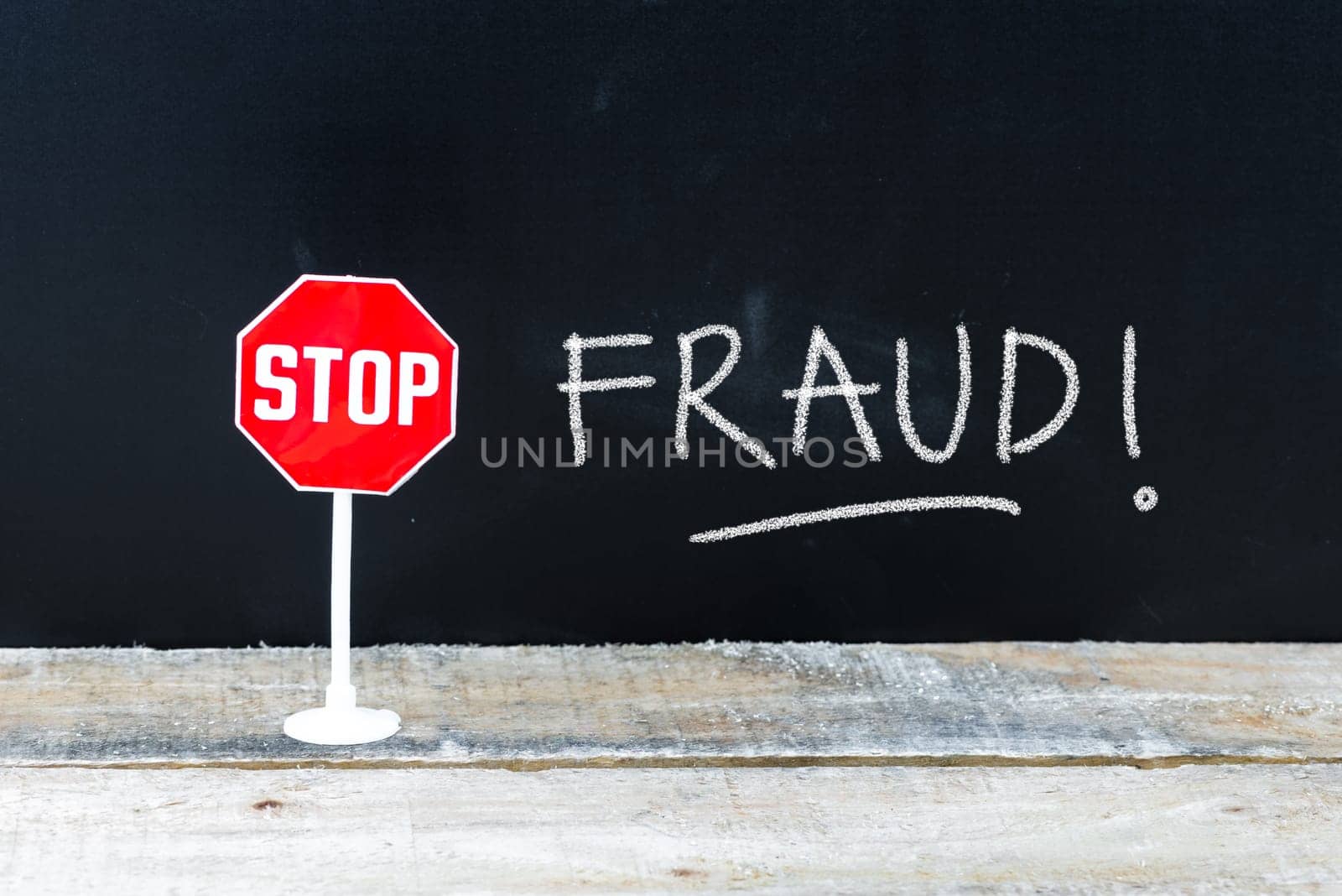 Mini STOP sign over chalkboard background and table, STOP FRAUD concept