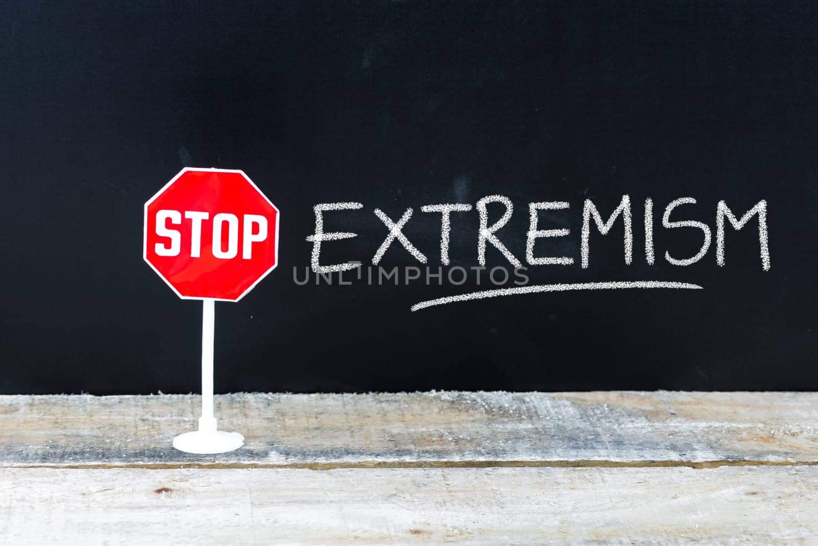 Mini STOP sign over chalkboard background and table, STOP EXTREMISM concept