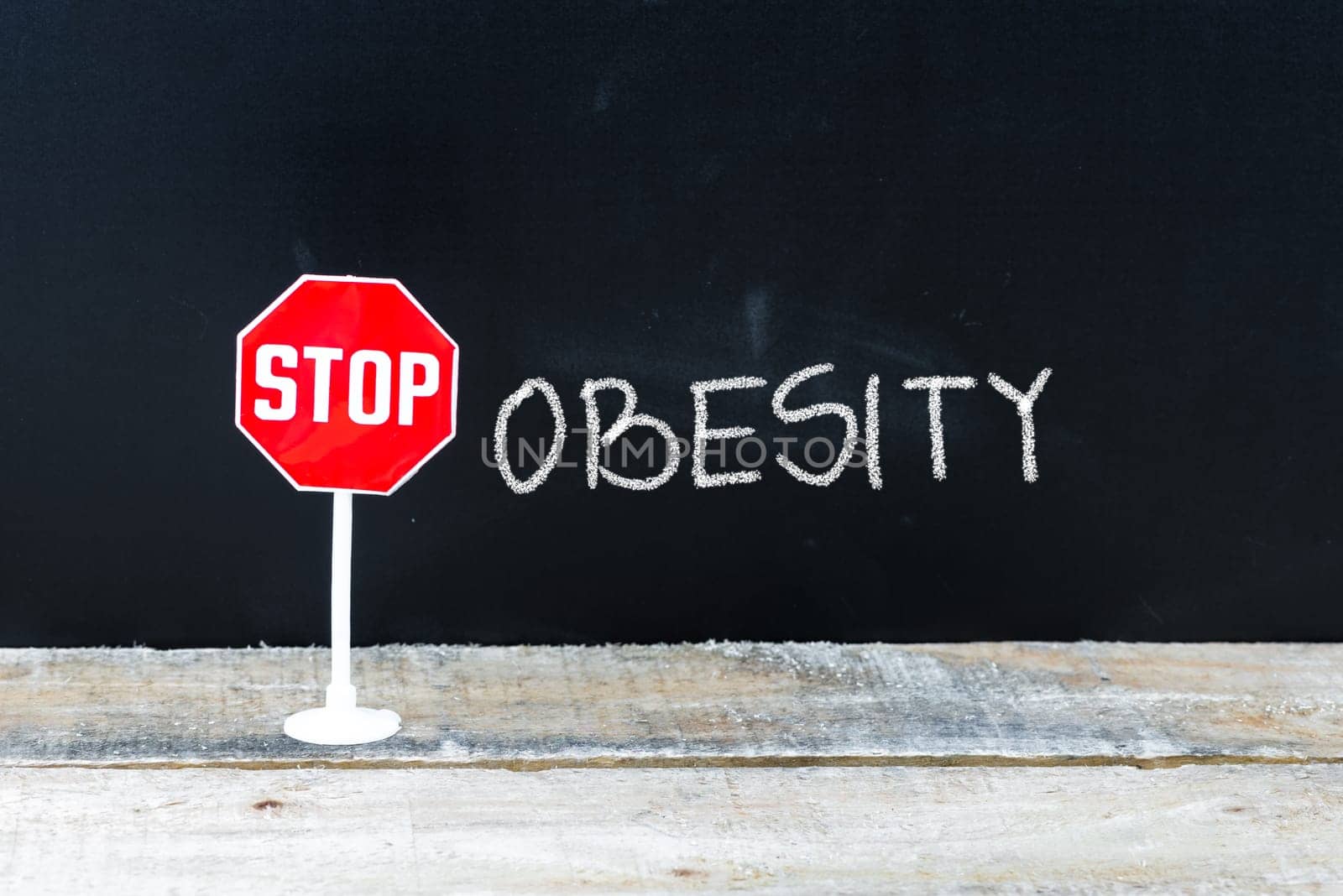 Mini STOP sign over chalkboard background and table, STOP OBESITY concept