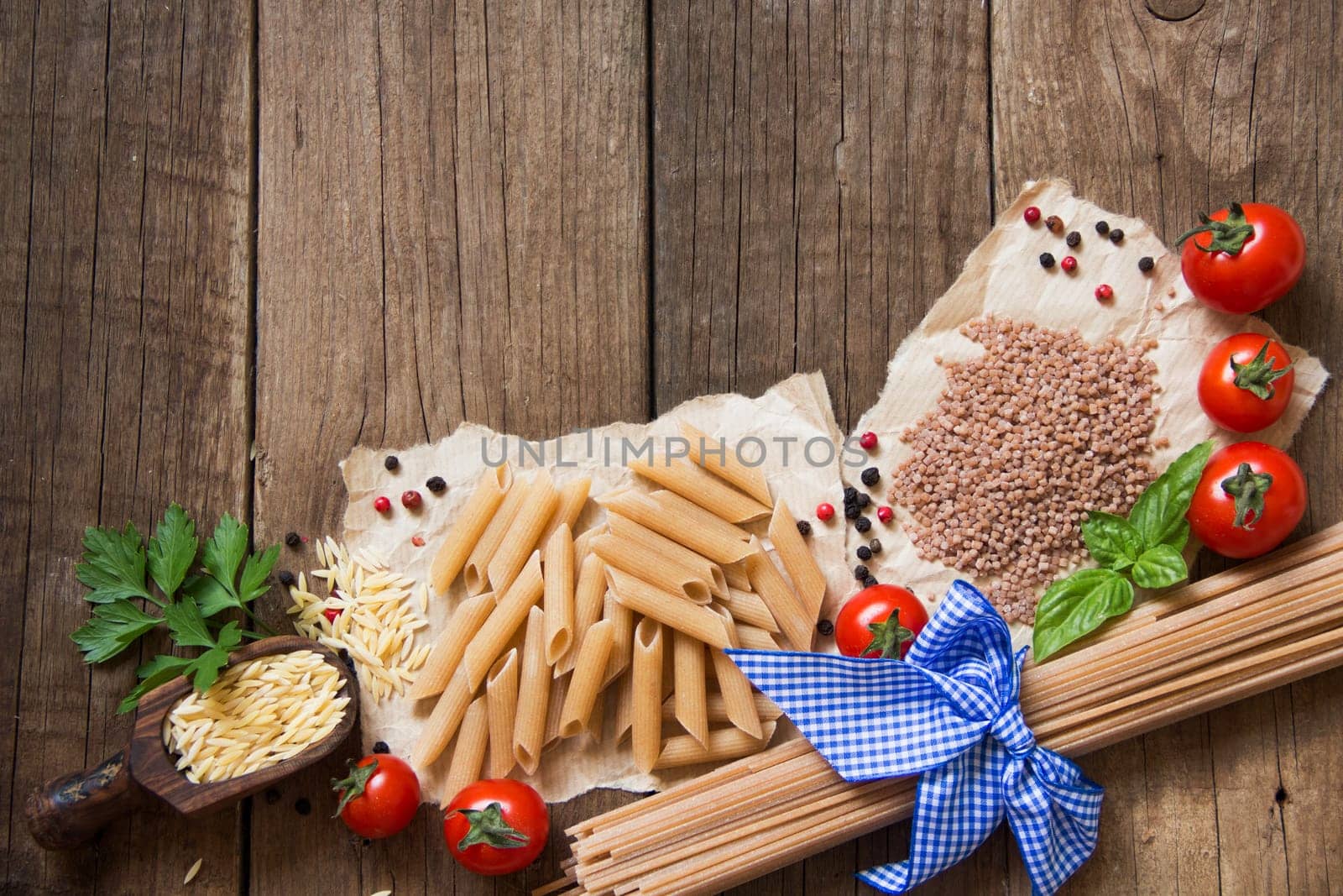 Pasta, tomatoes, basil and parsley on wooden background