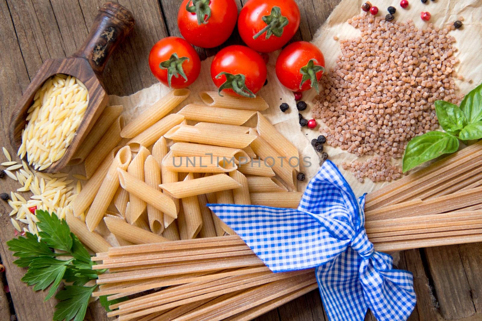 Pasta, tomatoes, basil and parsley on wooden background