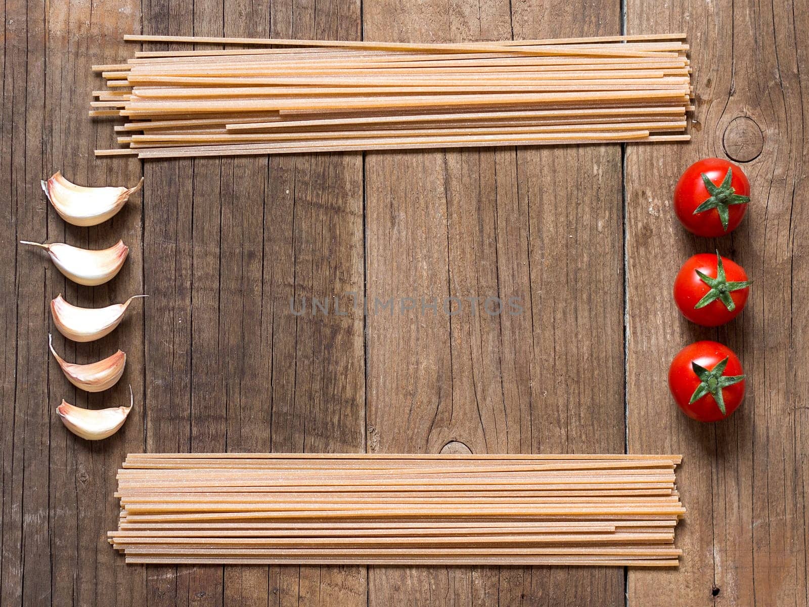 Pasta, tomatoes and garlic on wooden background