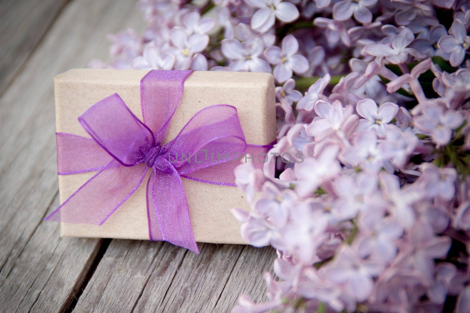 Gift box with purple bow and lilac on wood