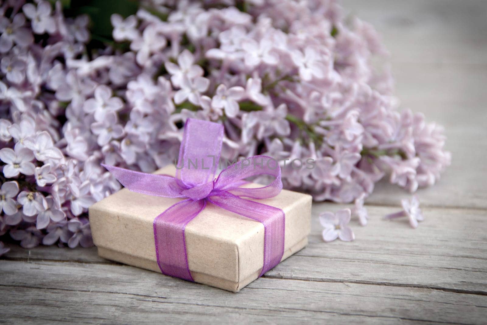 Gift box with purple bow and lilac on wood