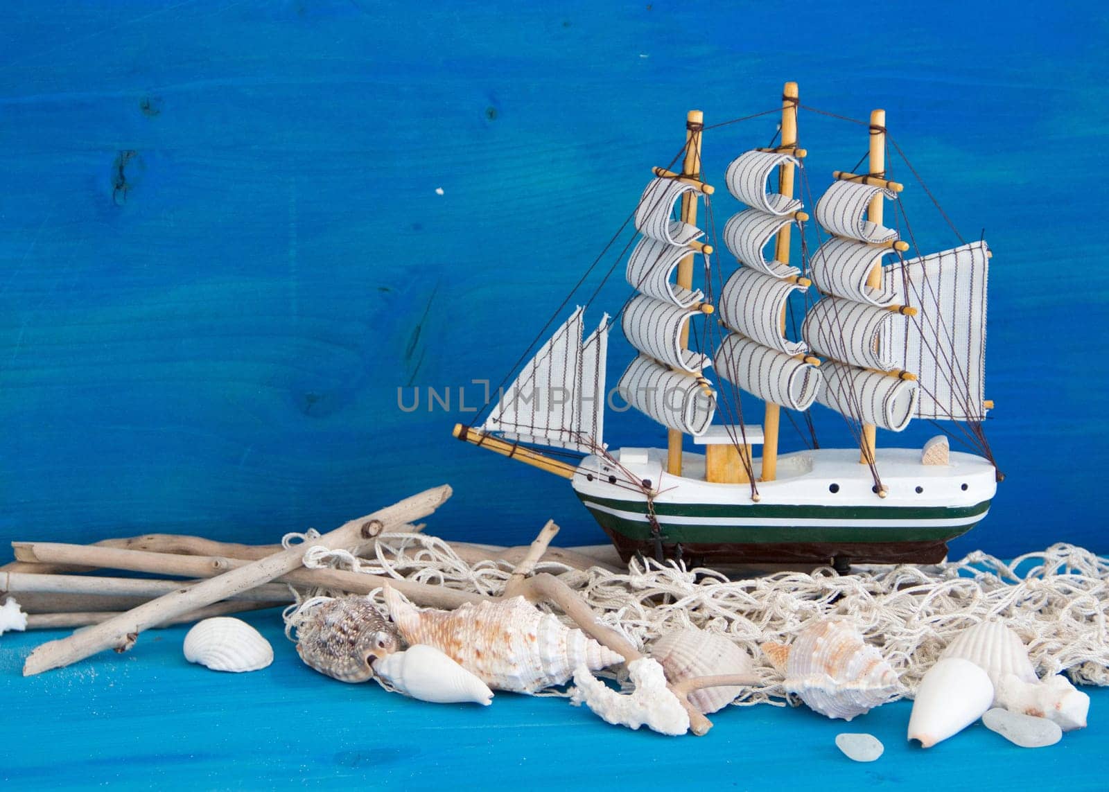 Toy sailboat, weathered wood and seashells on blue wood