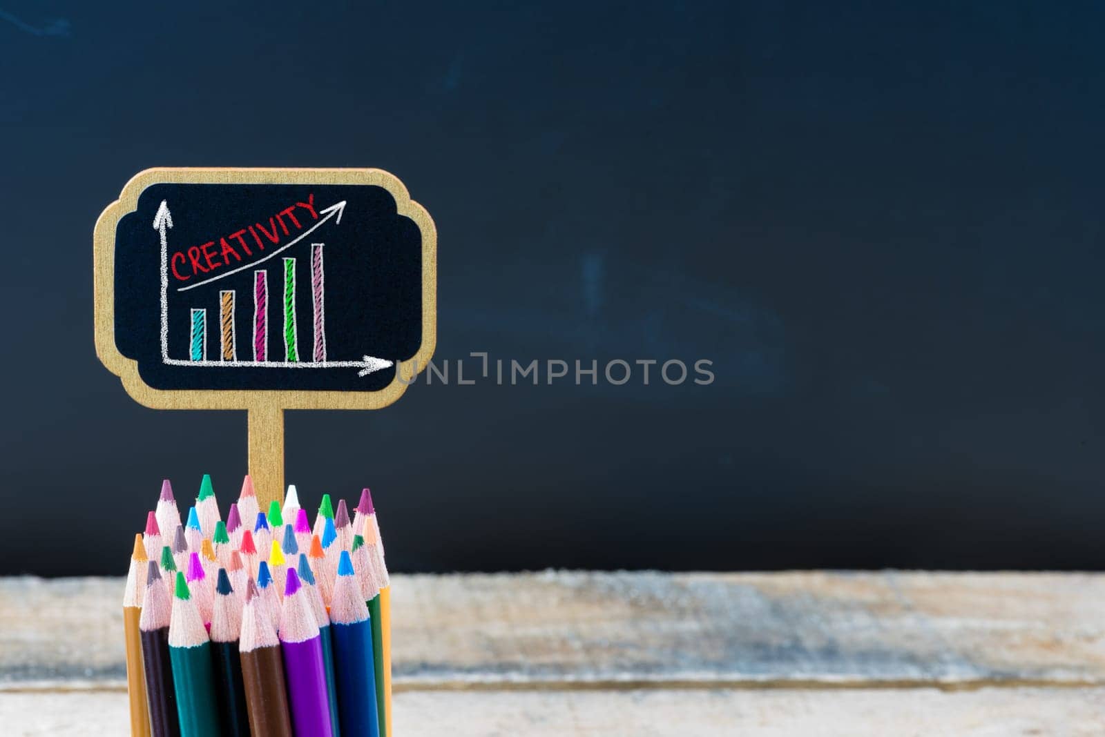 Wooden mini blackboard label with message Creativity and colouring pencils over chalkboard background, copy space available, education concept