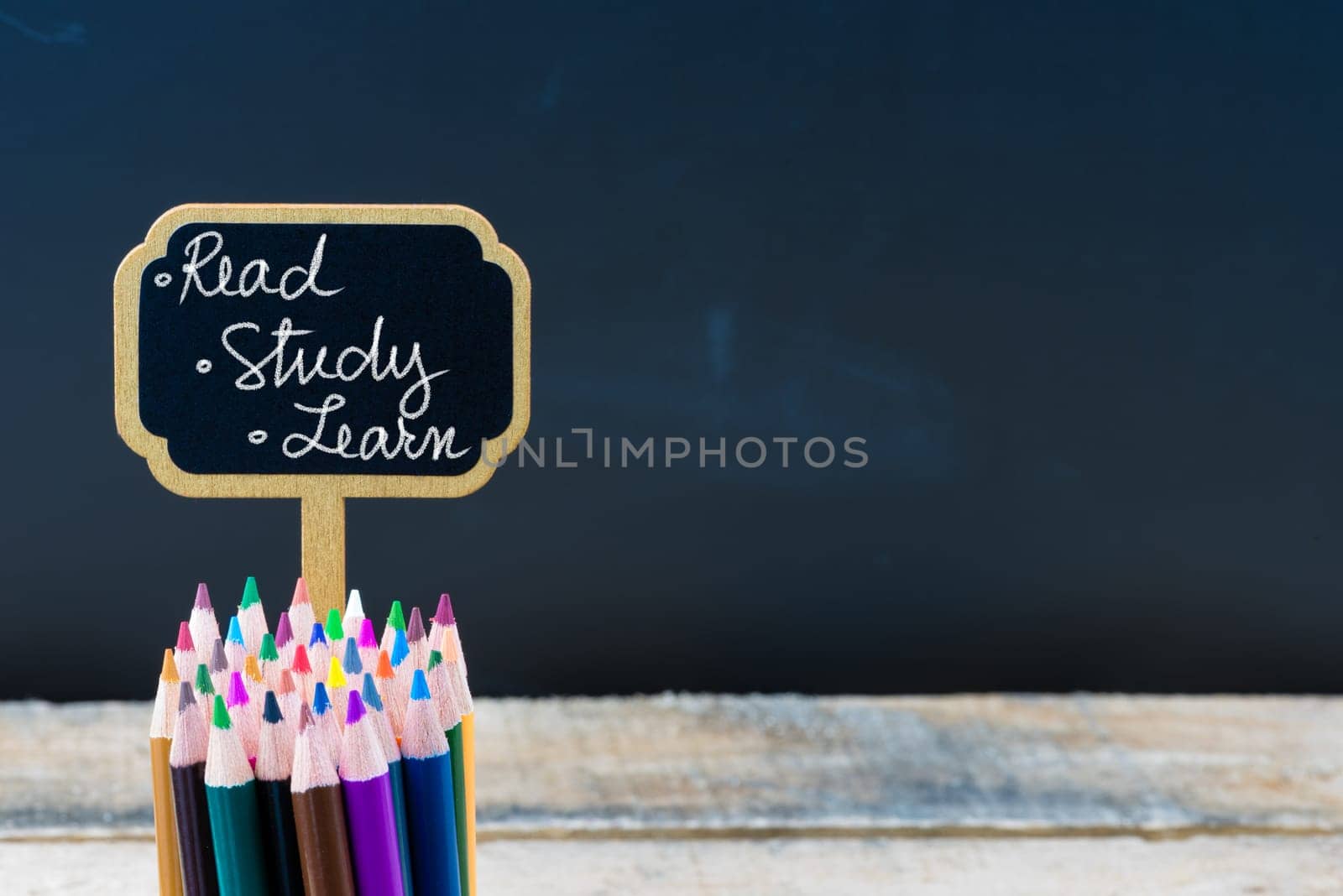 Wooden mini blackboard label with message Read, Study, Learn and colouring pencils over chalkboard background, copy space available, education concept