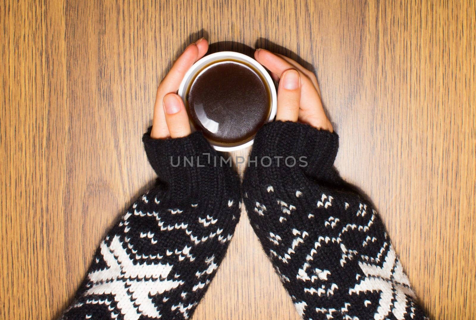 Woman hands in a woolen sweater holding a cup of coffee on wooden background