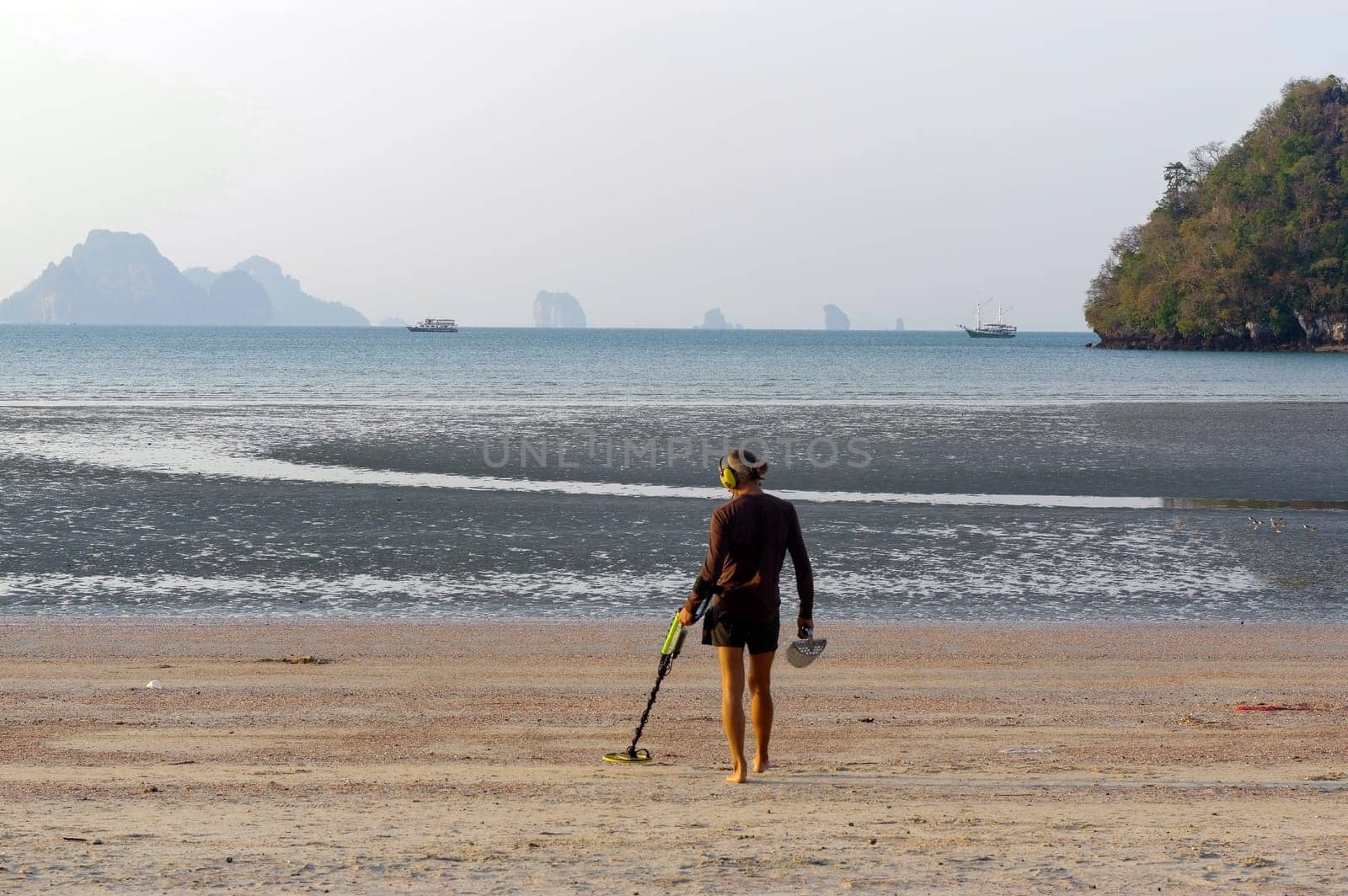 a treasure hunter with Metal detector on sunrise on the beach