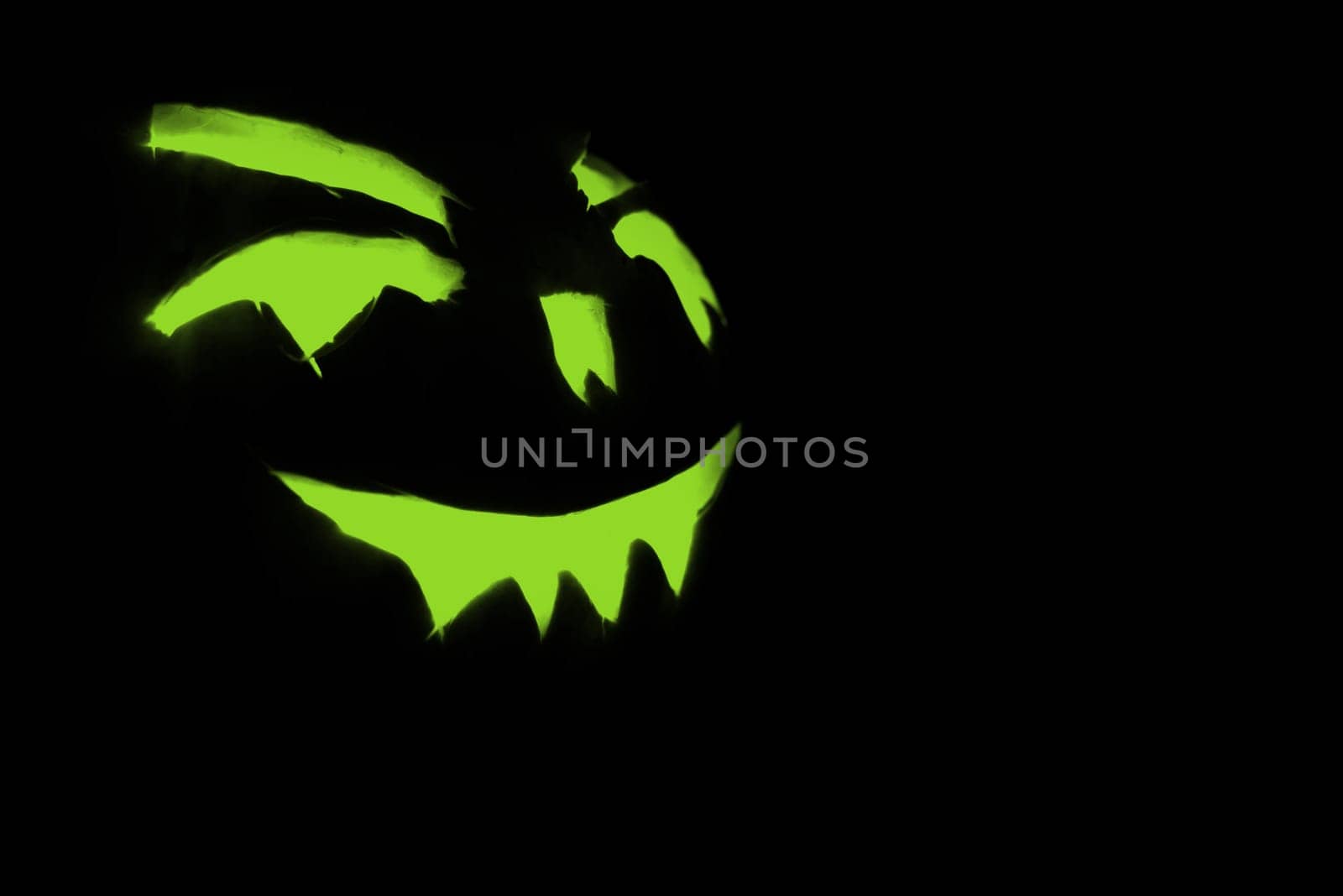 green carved face of pumpkin glowing on halloween black background