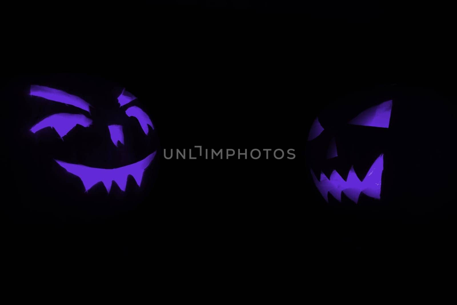 two blue carved face of pumpkin glowing on halloween black background