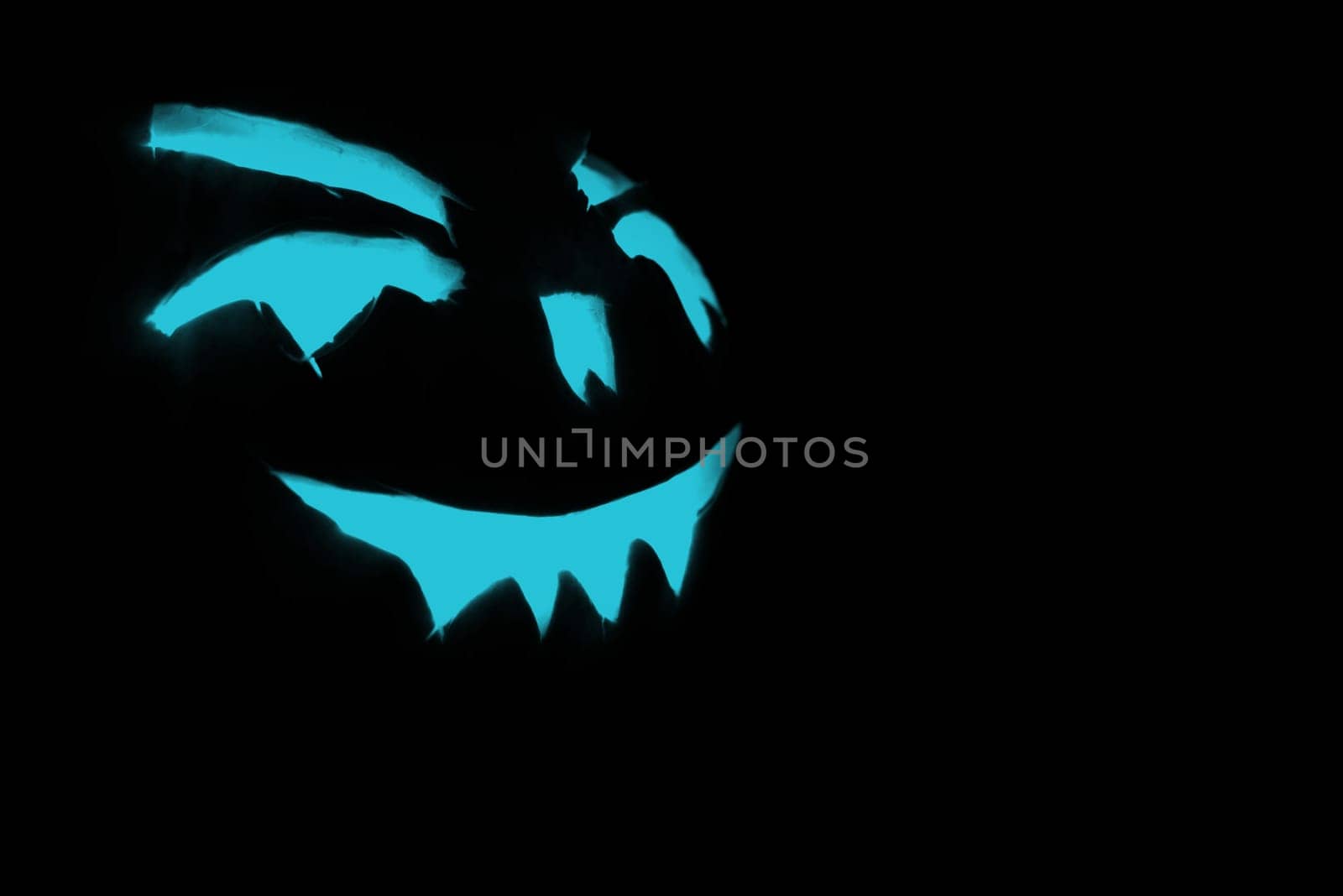 blue carved face of pumpkin glowing on halloween black background