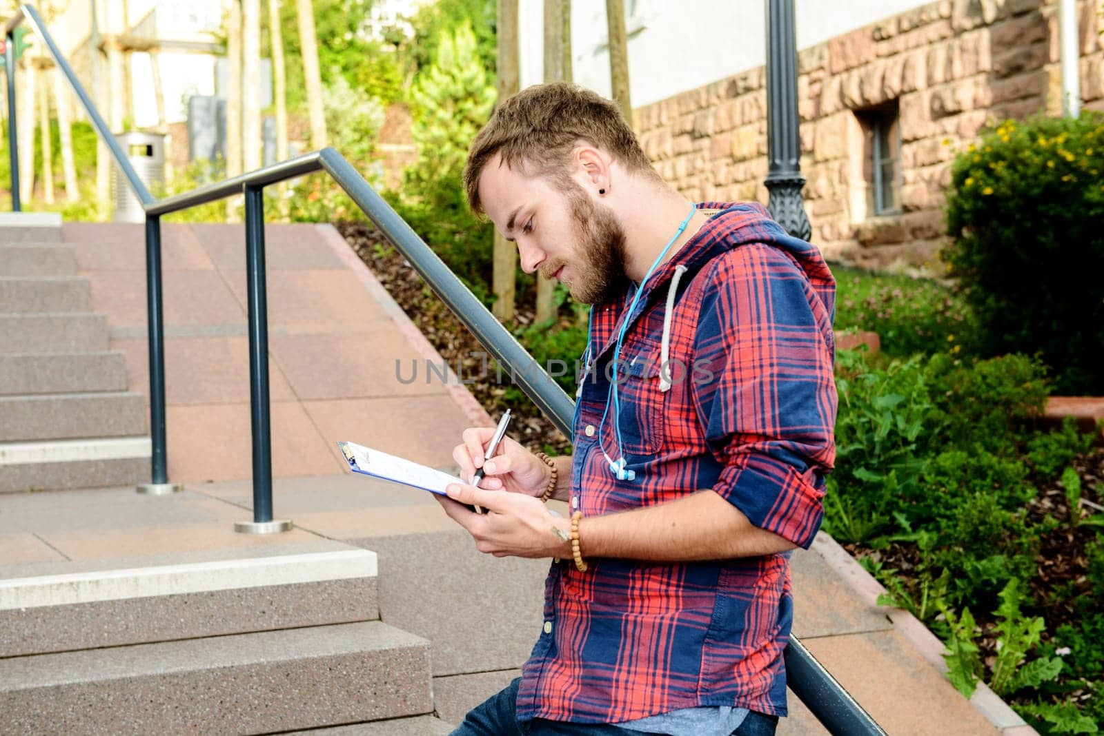 young man bearded standing by stairs with clipboard and writing