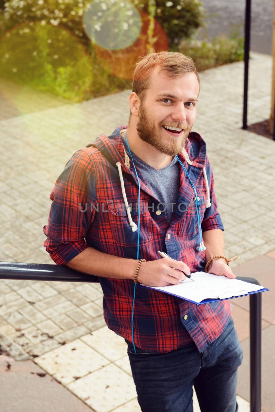 young man bearded standing by stairs with clipboard and writing