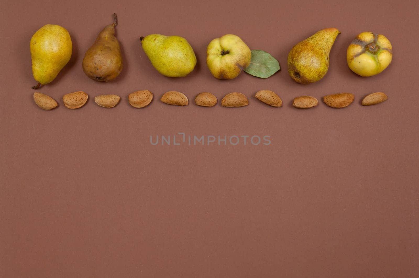 Pears and quince in shell almonds in row on yellow background with copy space