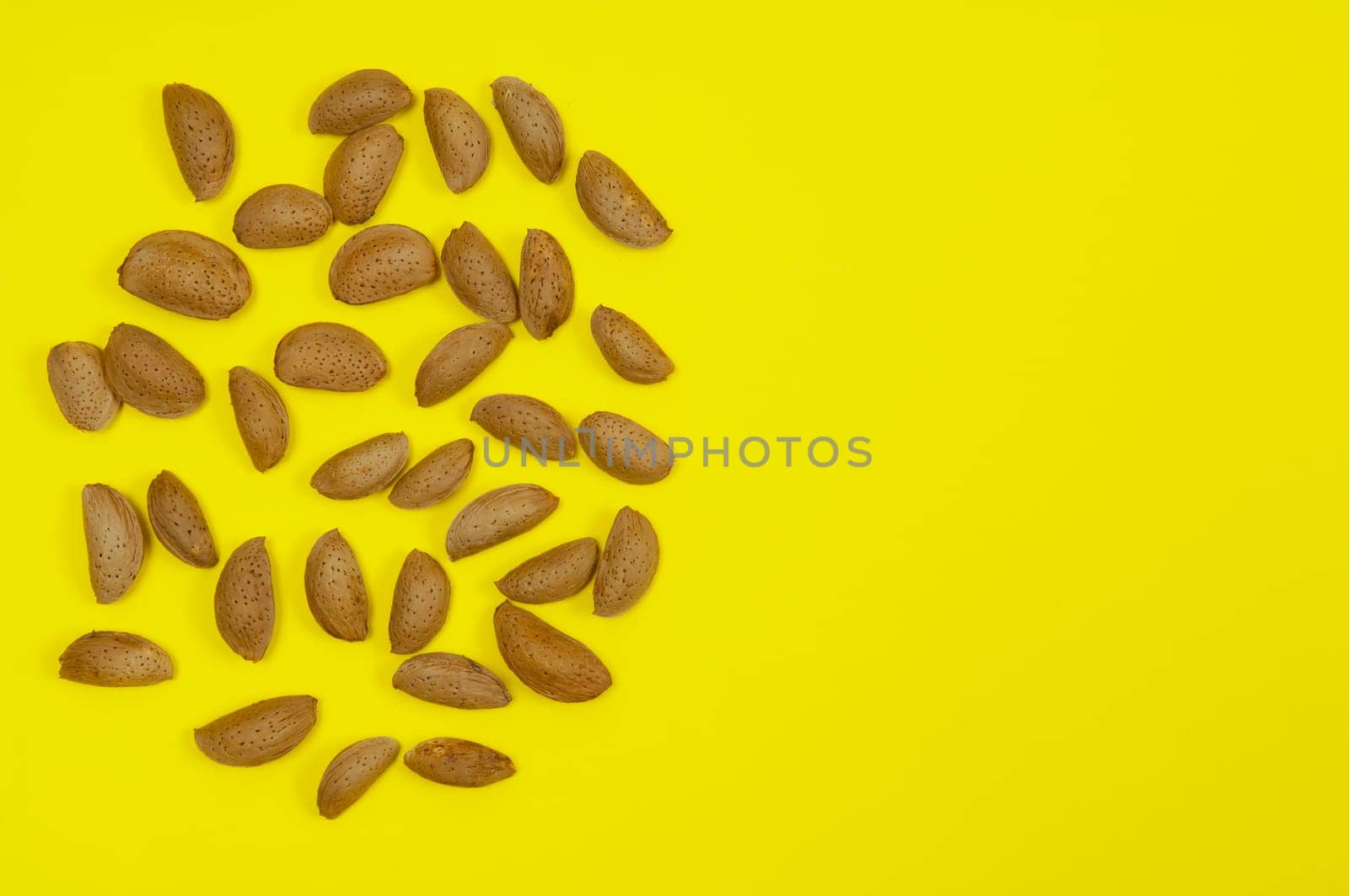 A pile of in shell raw almond on yellow background with copy space