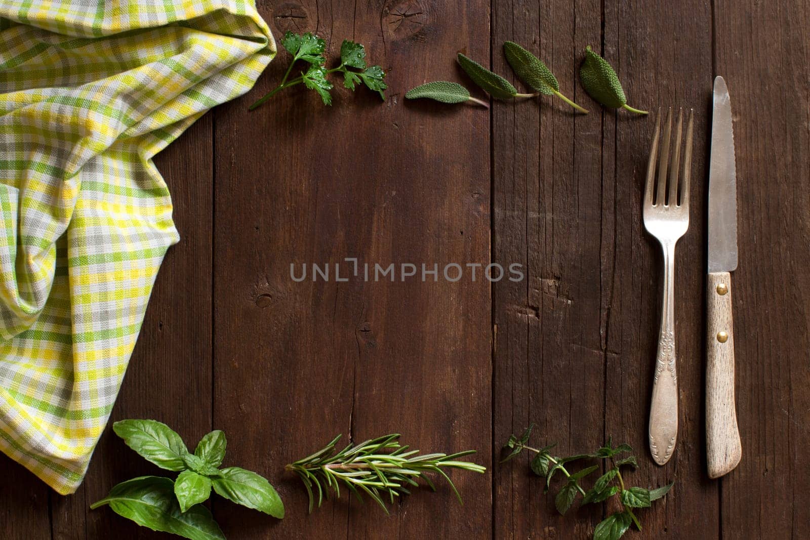Herbs, napkin, fork and knife on a wooden table top view