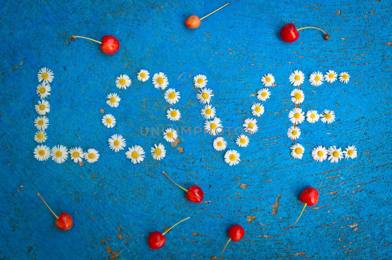 The word Love written of daisy flowers on textured blue background, top view