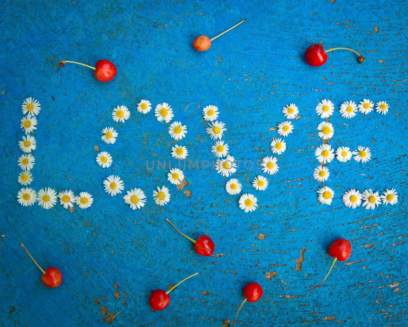 The word Love written of daisy flowers on textured blue background, top view