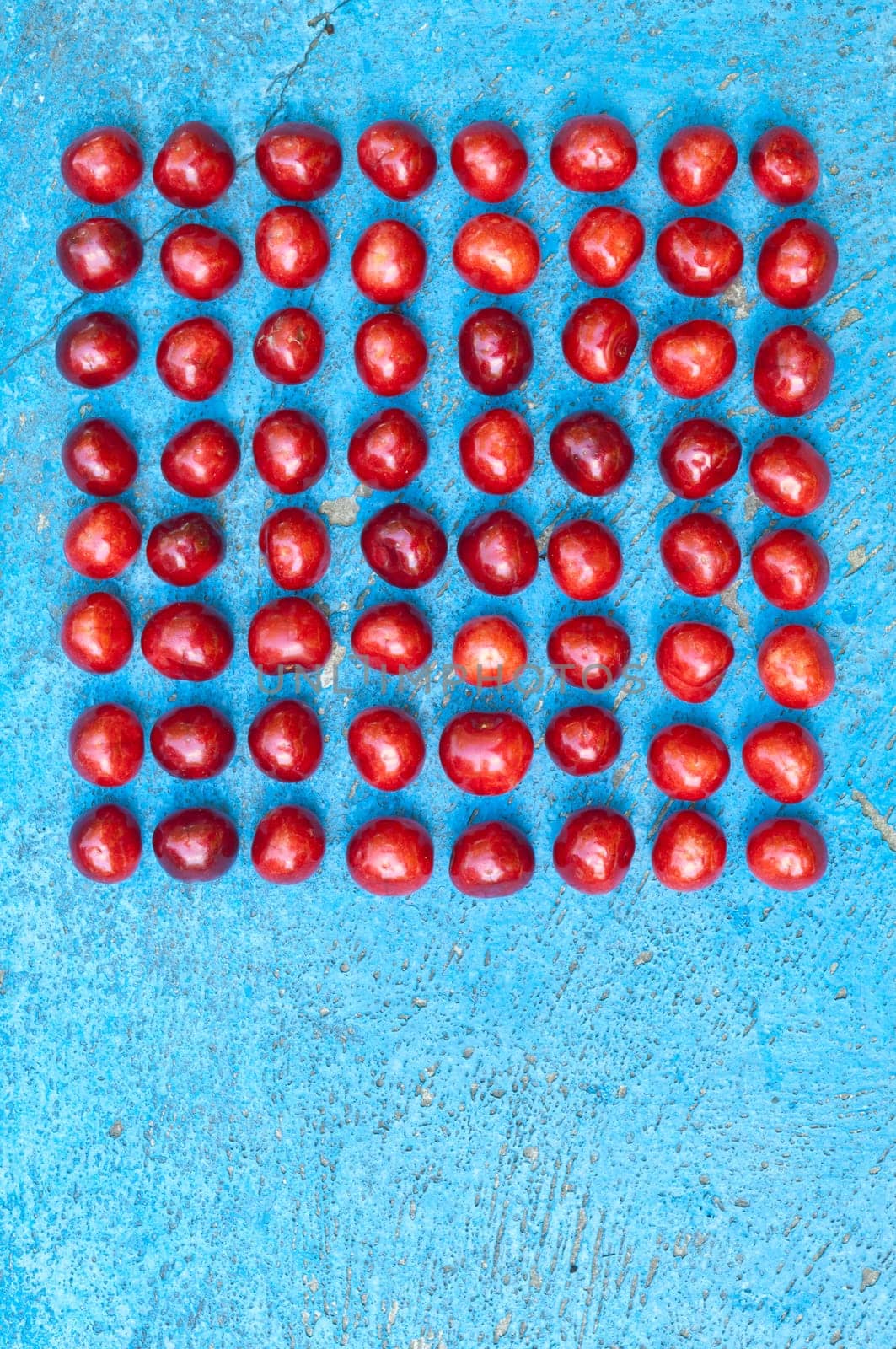 Square arrangement of ripe cherries on blue textrured background, cherry pattern