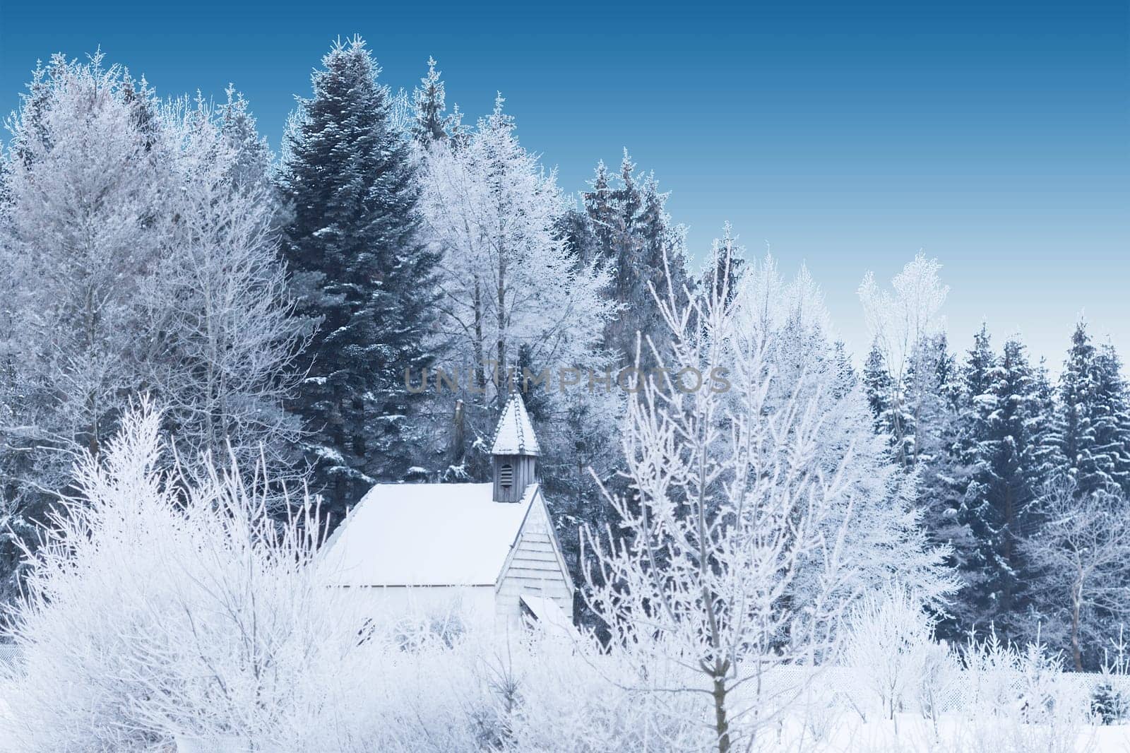 Snow-capped little wooden chapel in frosty winter forest. Tranquil beautiful view in Germany Bavaria province Allgaeu with deep blue sky.